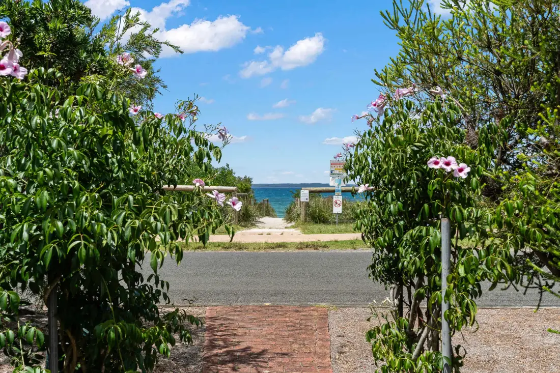 A garden path leads toward the beach, framed by flowering shrubs.