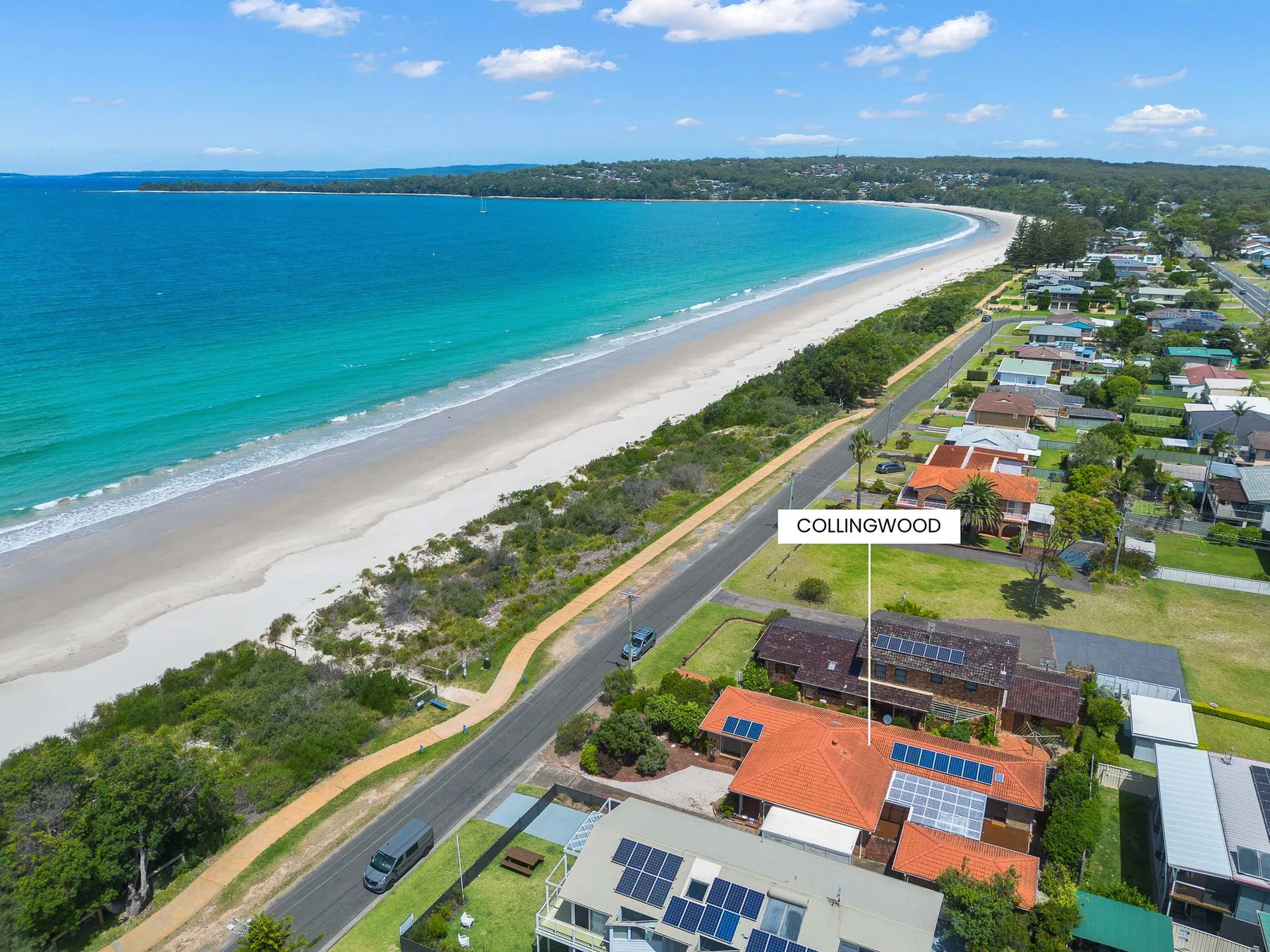 Aerial view of a coastal beach, turquoise water, and nearby homes.