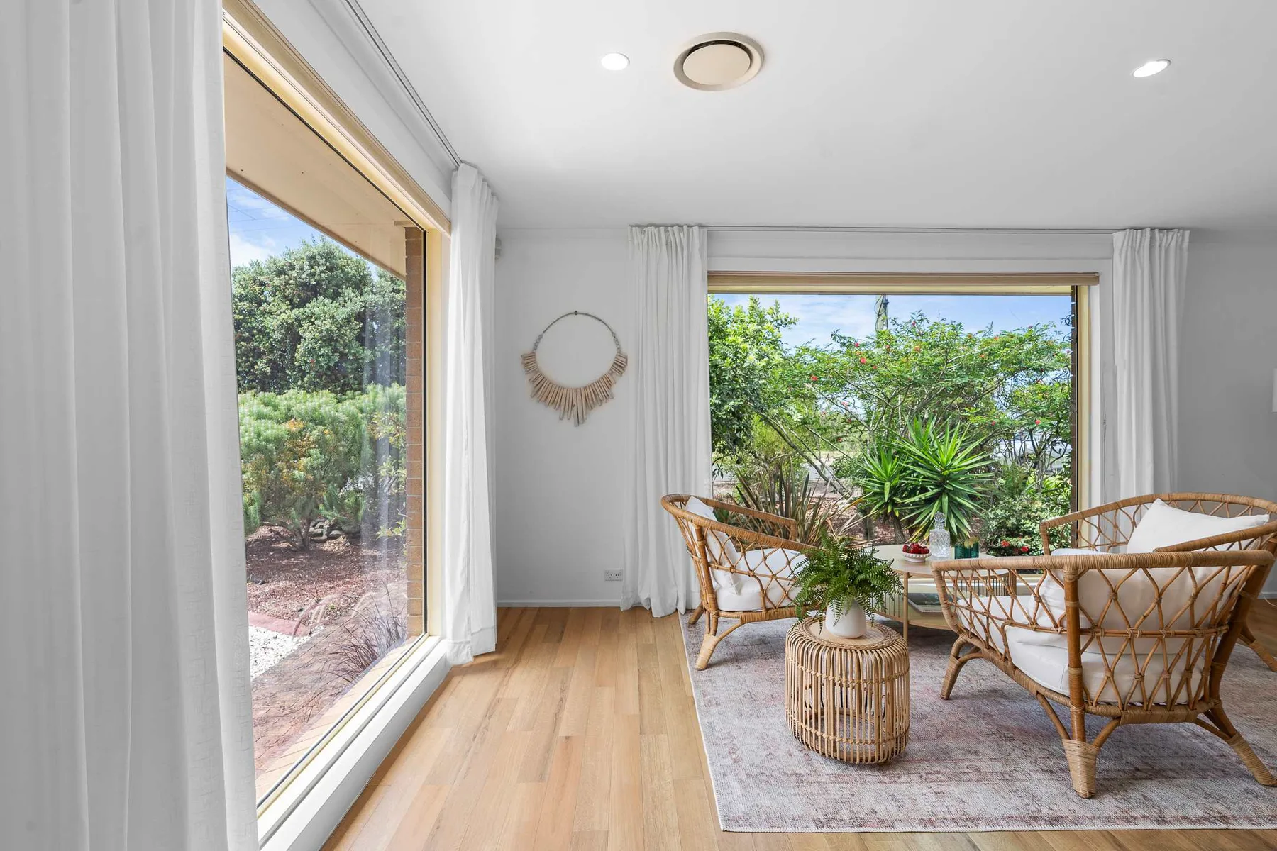 A bright sunroom with rattan seating beside large windows overlooking greenery.