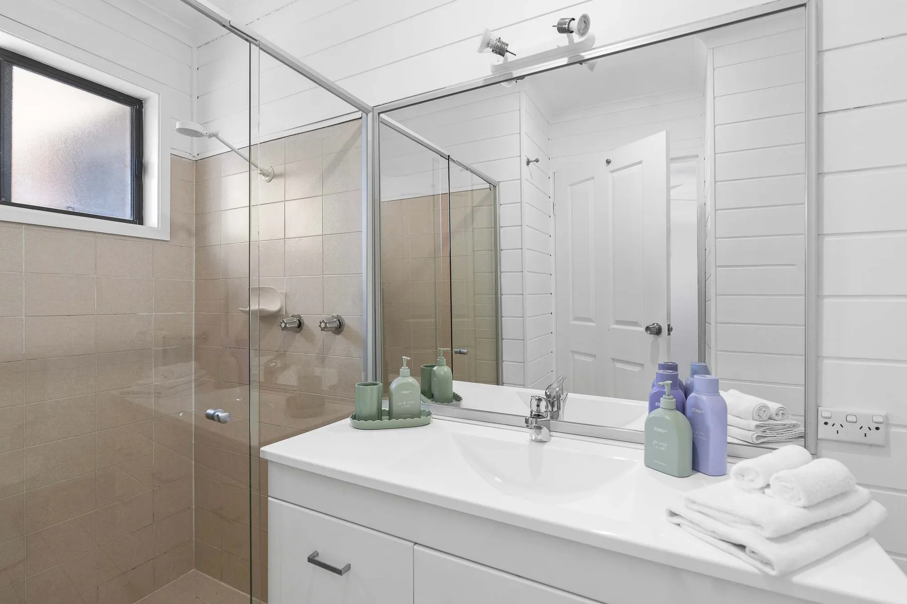 A bright bathroom with a glass shower and a sink vanity.