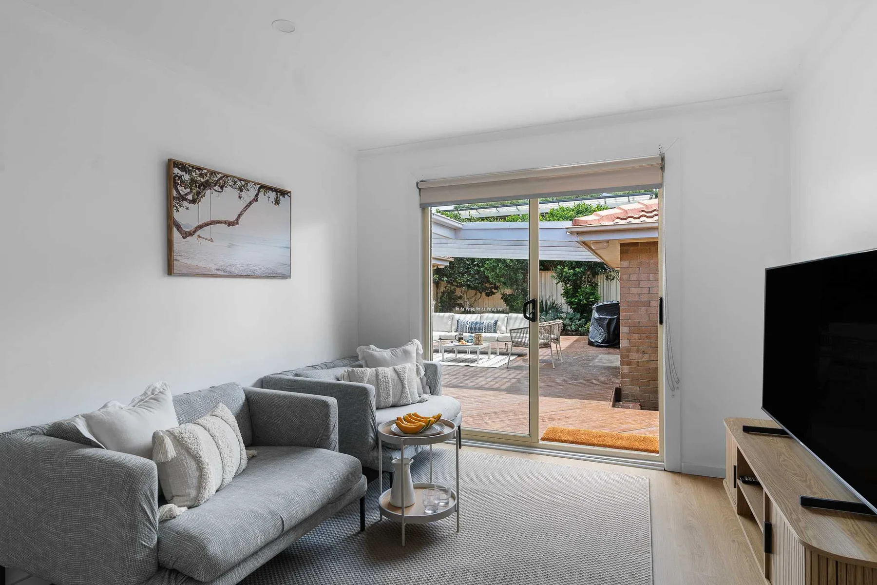 A bright living room with seating beside a sliding glass door opening onto a patio.