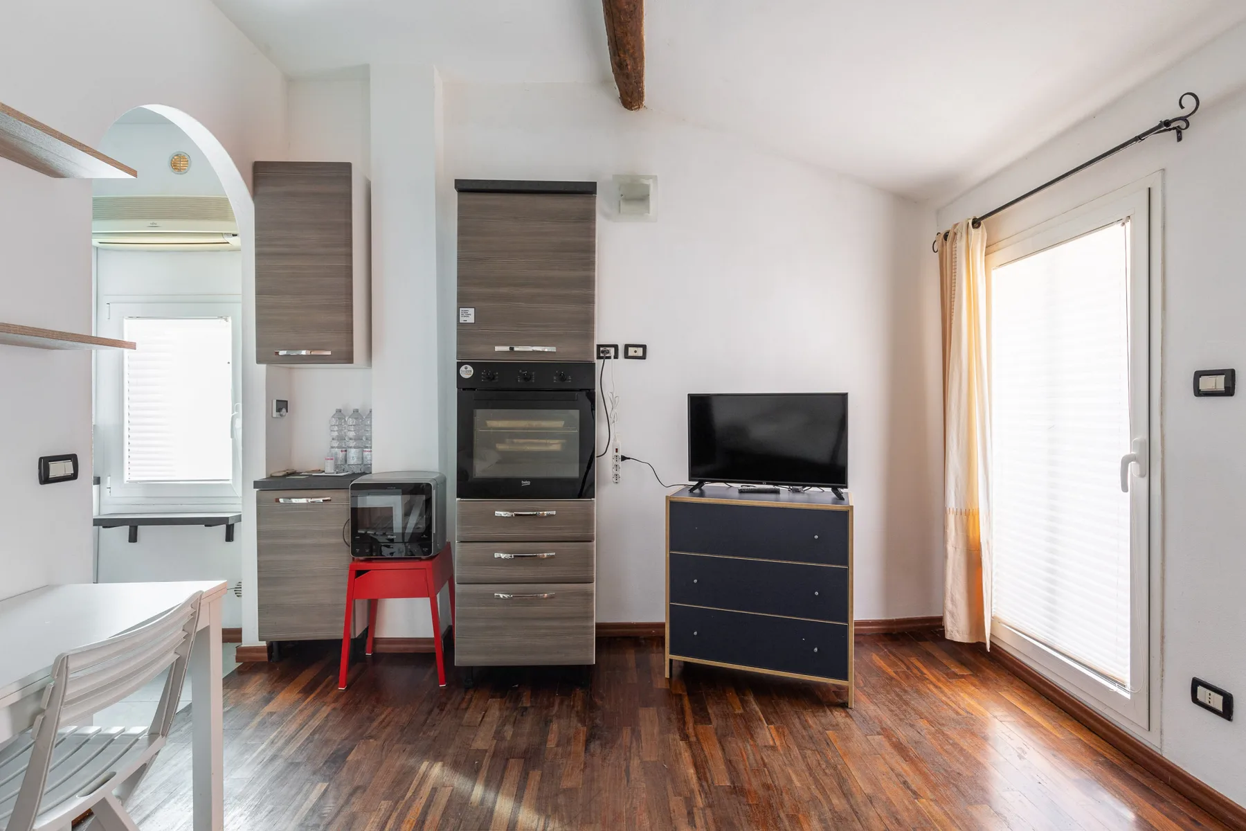 Una luminosa sala de estar con un televisor sobre un mueble bajo junto a grandes puertas de vidrio.
