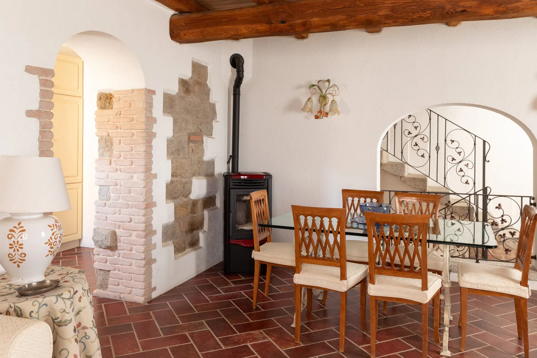 Comedor rústico con asientos de madera y una escalera detrás de un arco.