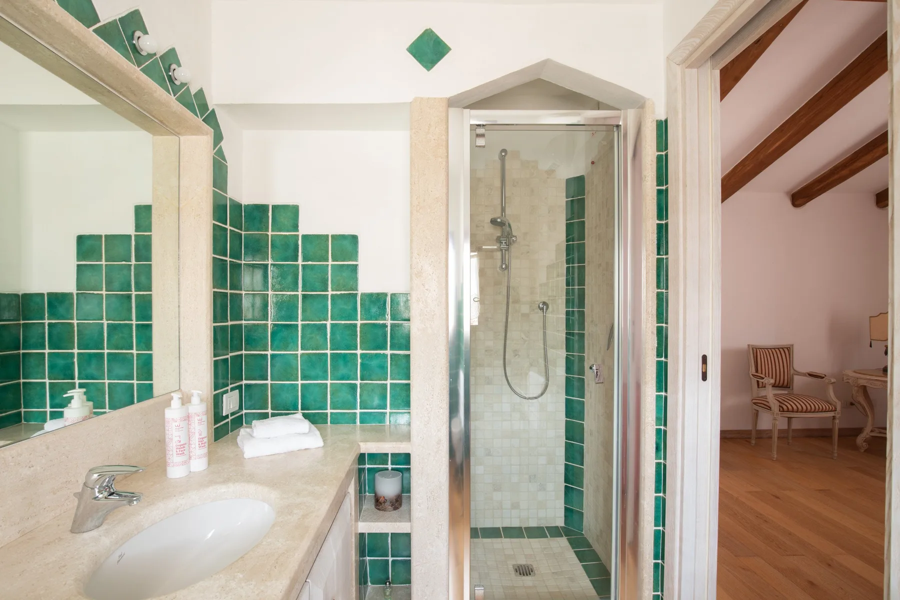 Un baño con azulejos tiene un lavabo y una ducha de vidrio junto a una puerta abierta.