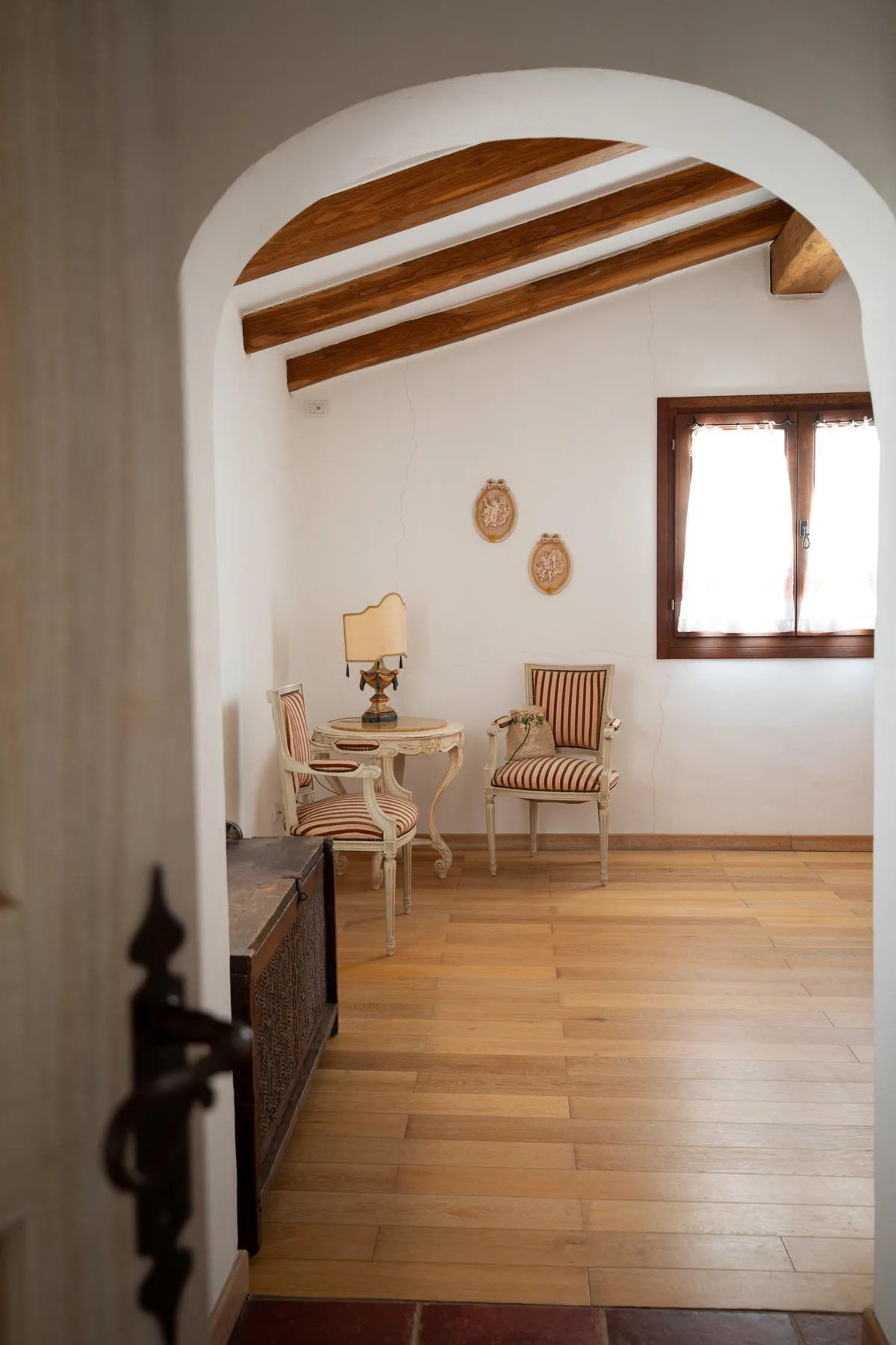 Una sala luminosa con vigas de madera en el techo, una ventana y una mesa pequeña.