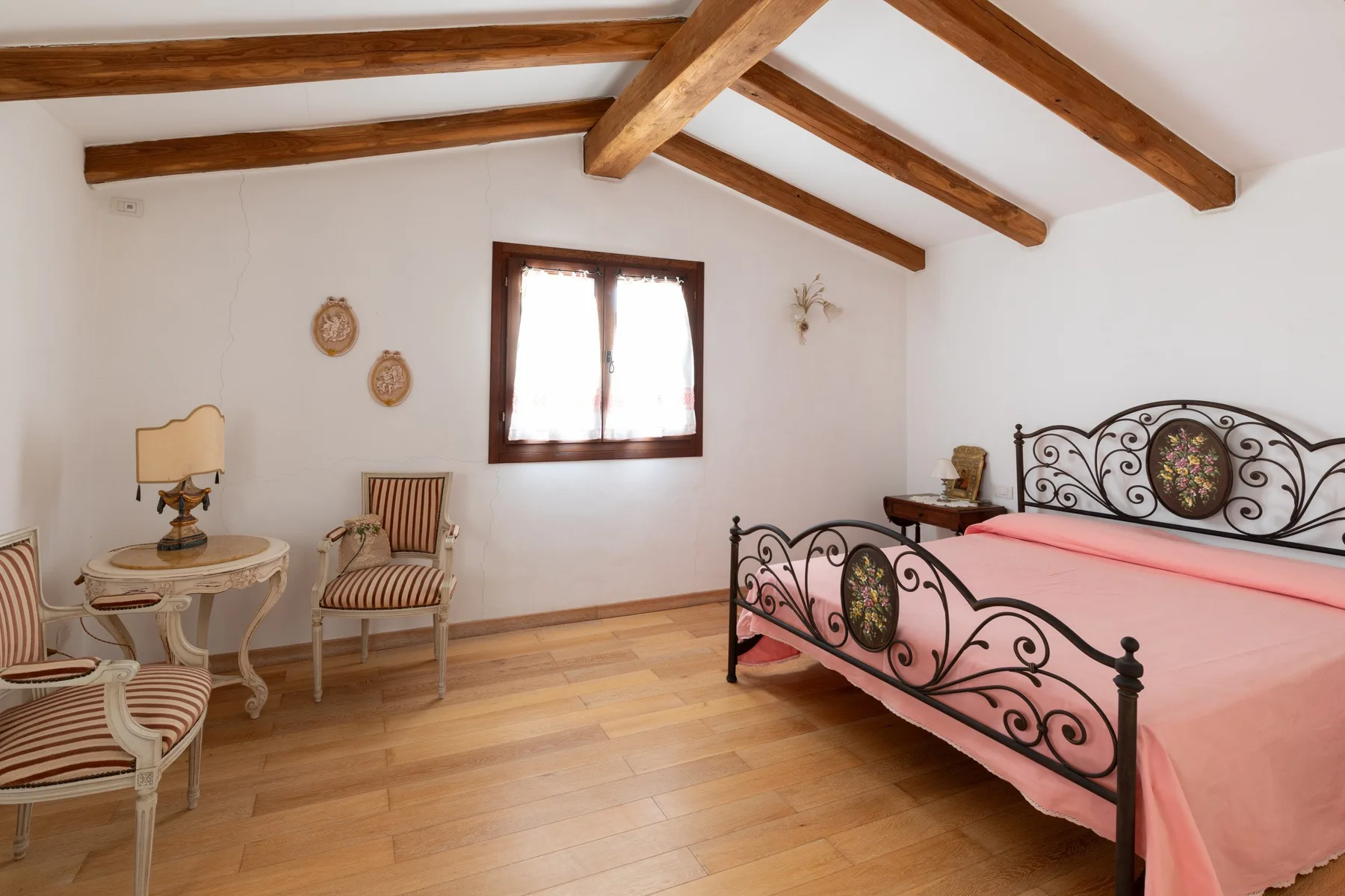 Un dormitorio con una cama cubierta de rosa, vigas de madera y una ventana.