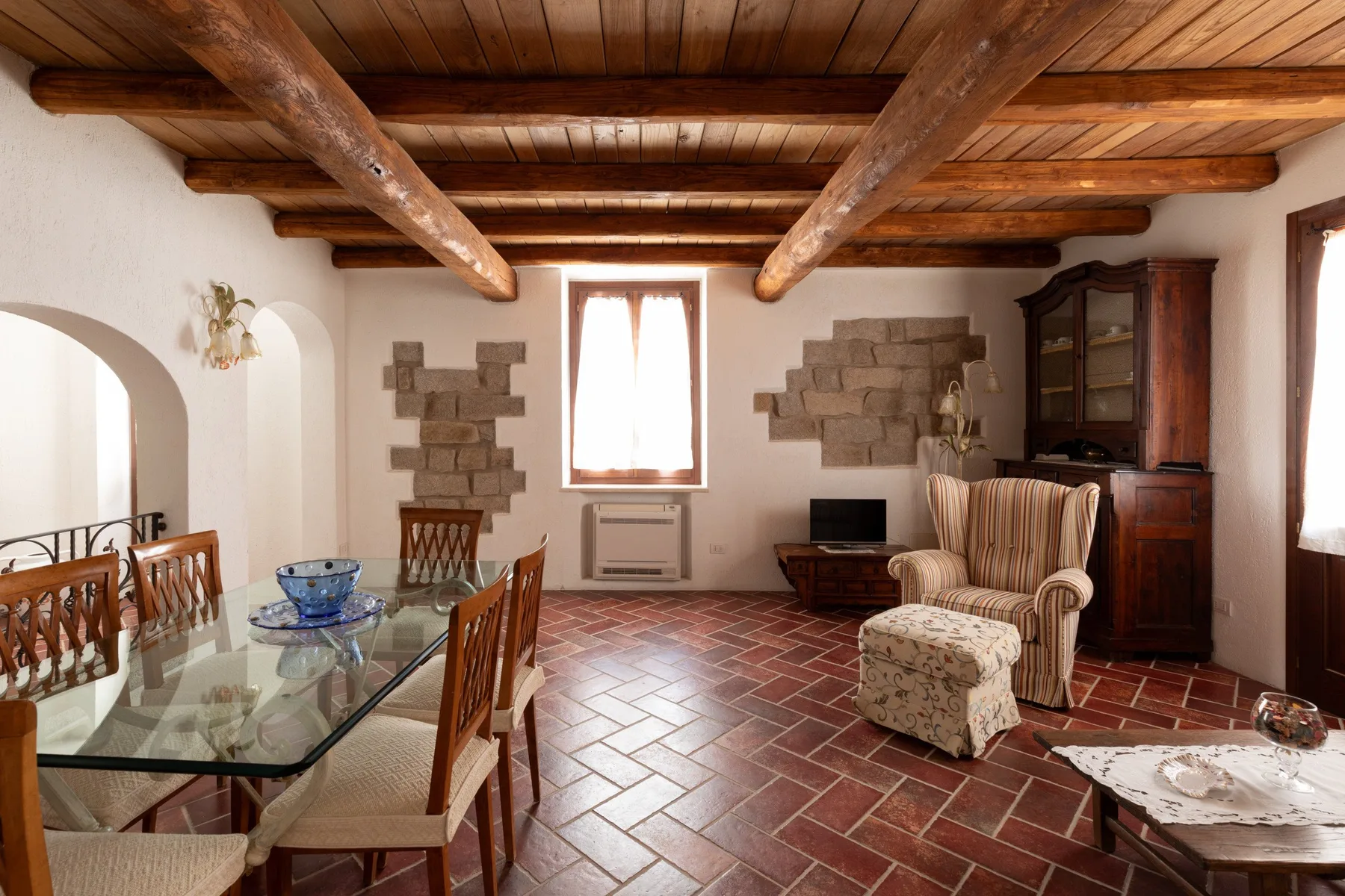 Una sala de estar y comedor rústica con techo de vigas de madera y suelo de baldosas.