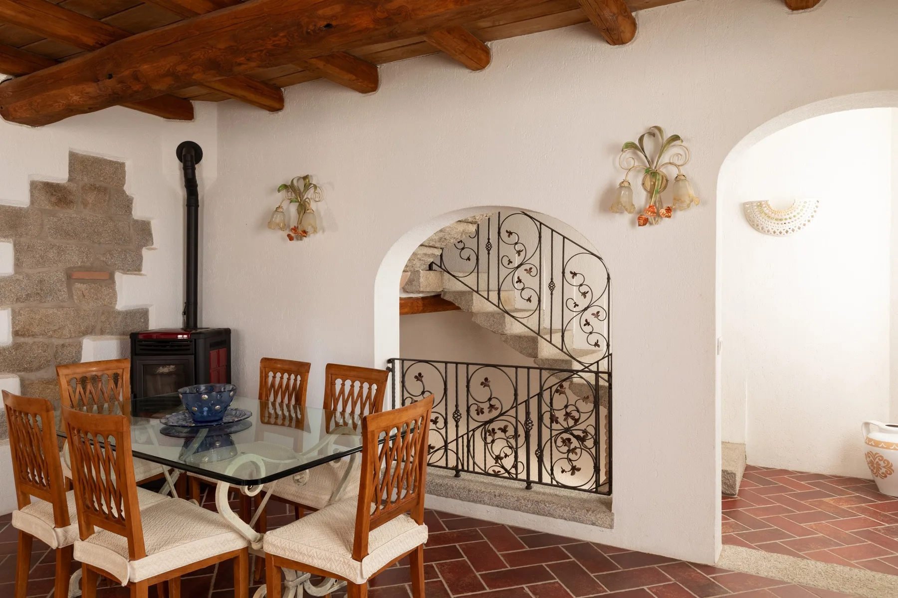 Un comedor con mesa de vidrio y asientos de madera está junto a una escalera.