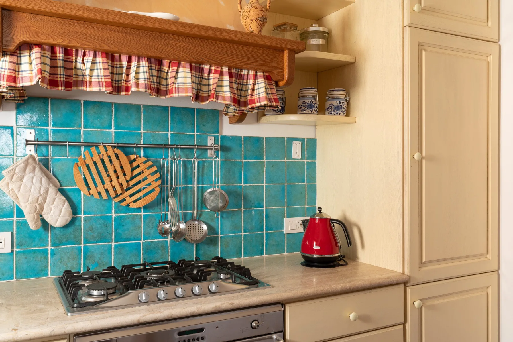 Una zona de cocina tiene una placa de gas, azulejos turquesa y una tetera roja.