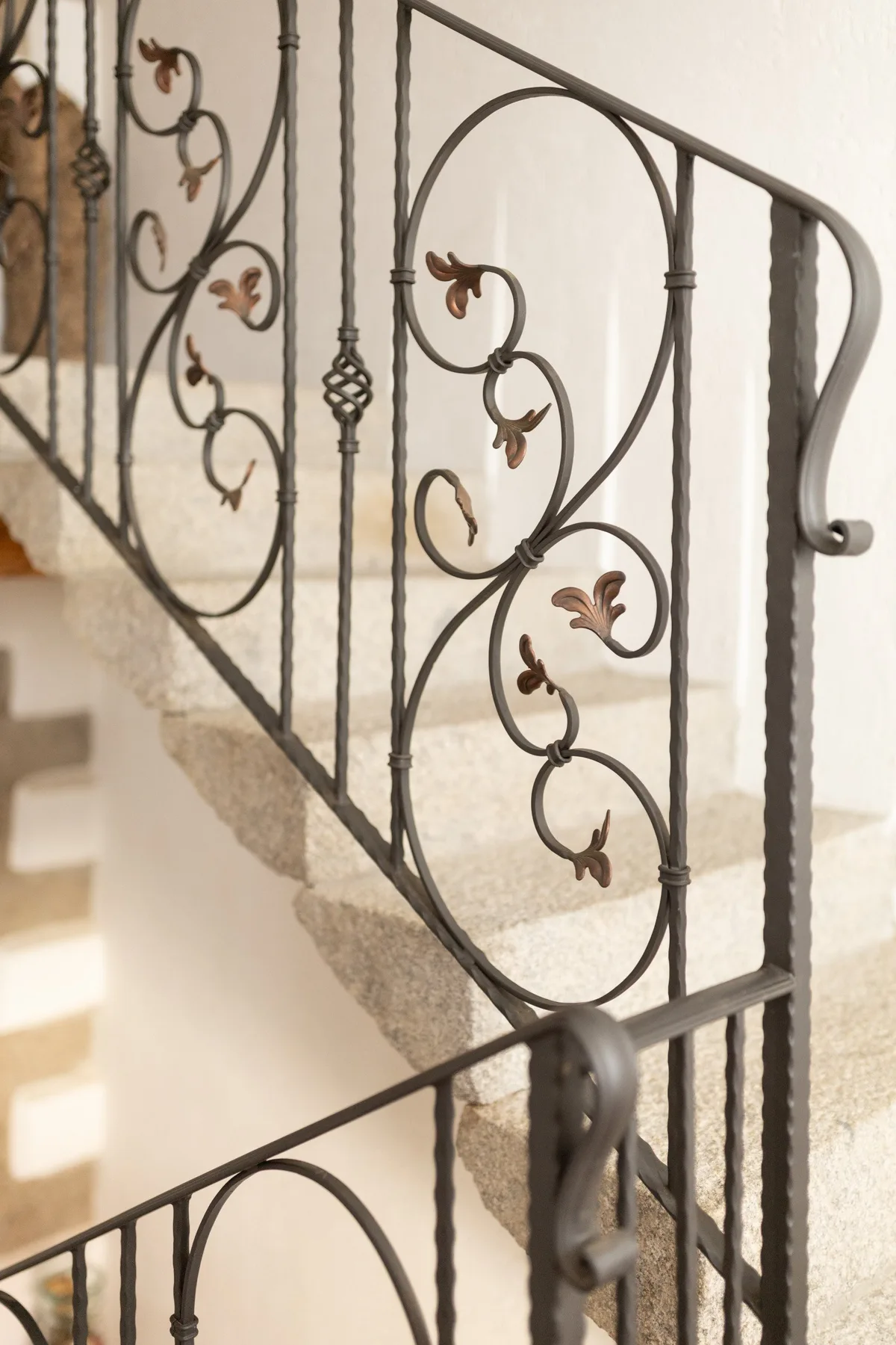 Una escalera interior con barandales decorativos de hierro y peldaños de piedra clara.