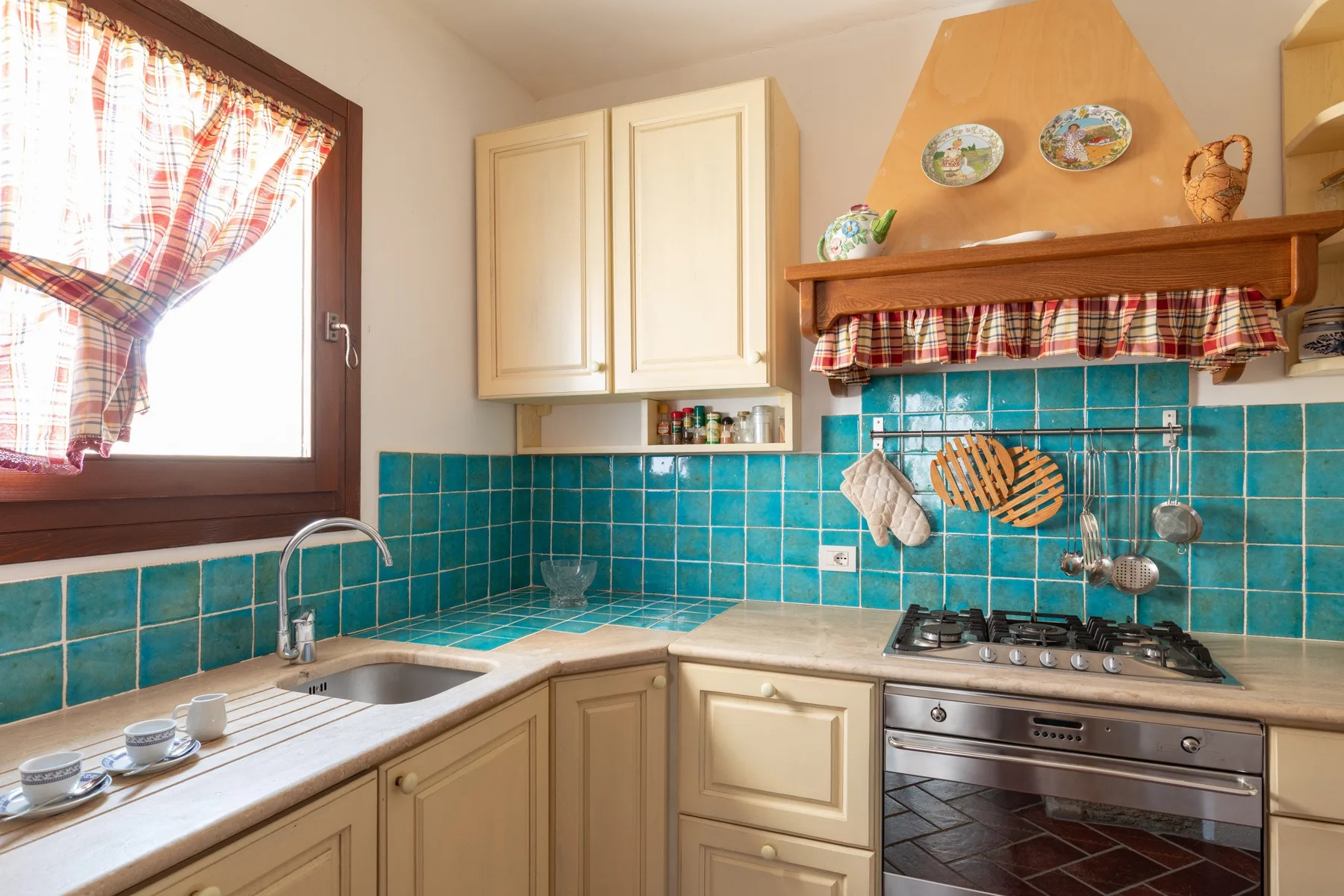 Una cocina con azulejos turquesa, gabinetes claros y una estufa bajo una campana de madera.