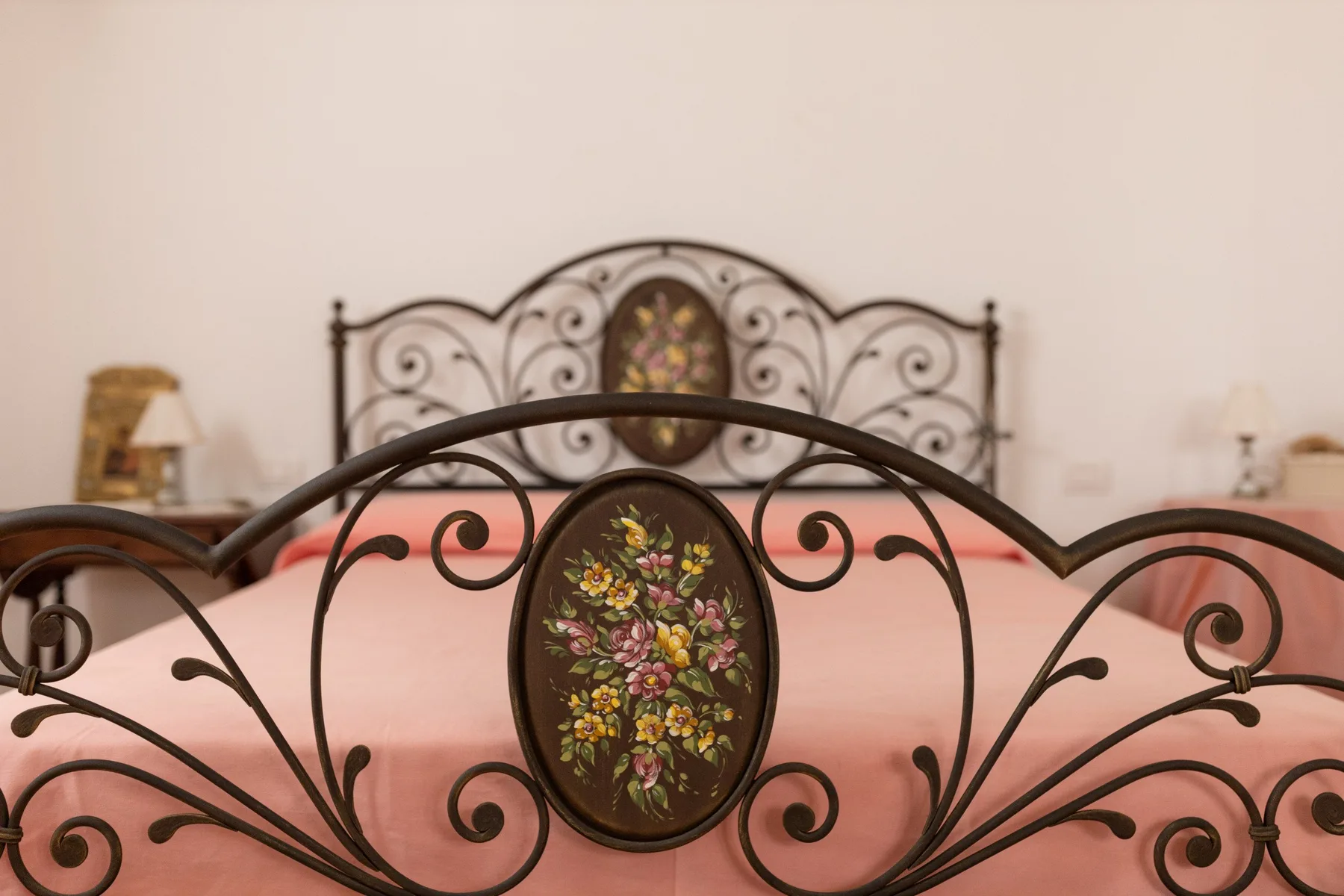 Un dormitorio con camas de metal oscuro ornamentadas y adornos florales.