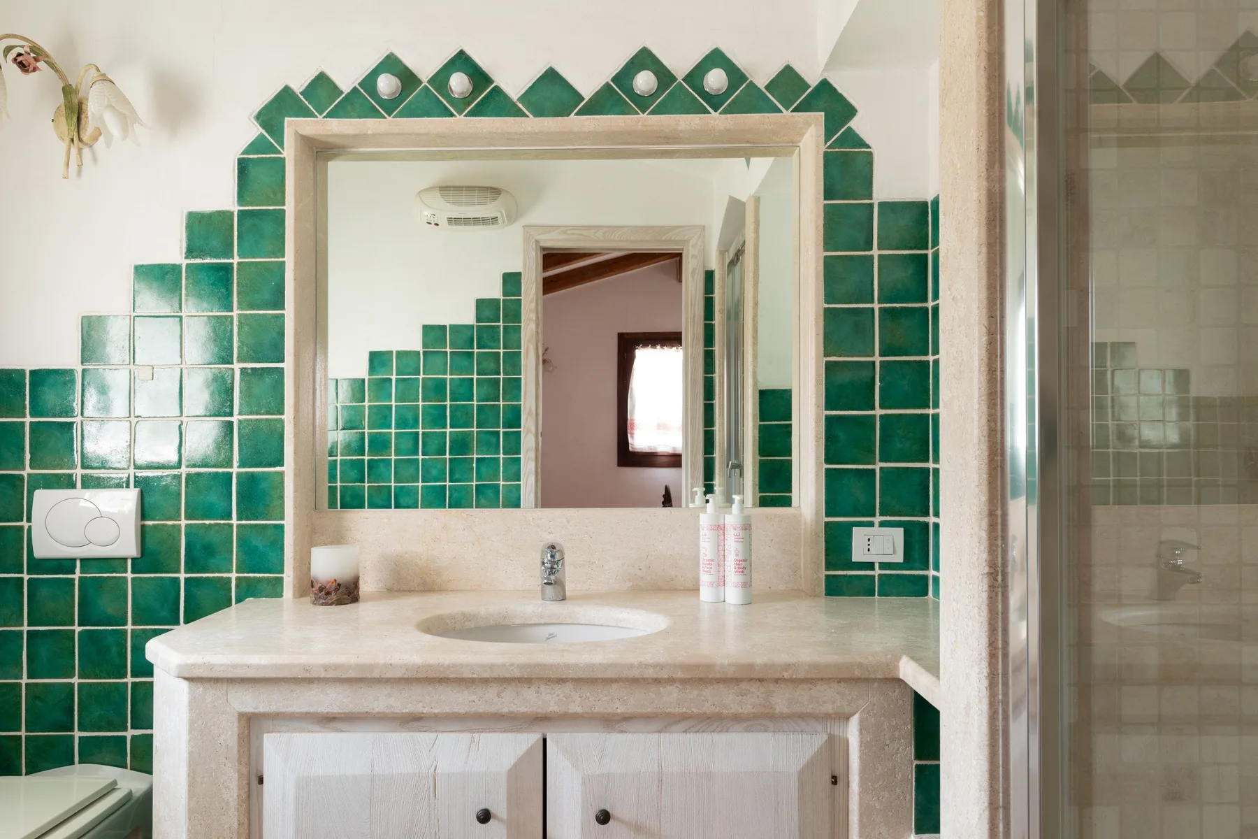 Un lavabo de baño con espejo está frente a una pared de azulejos verdes.