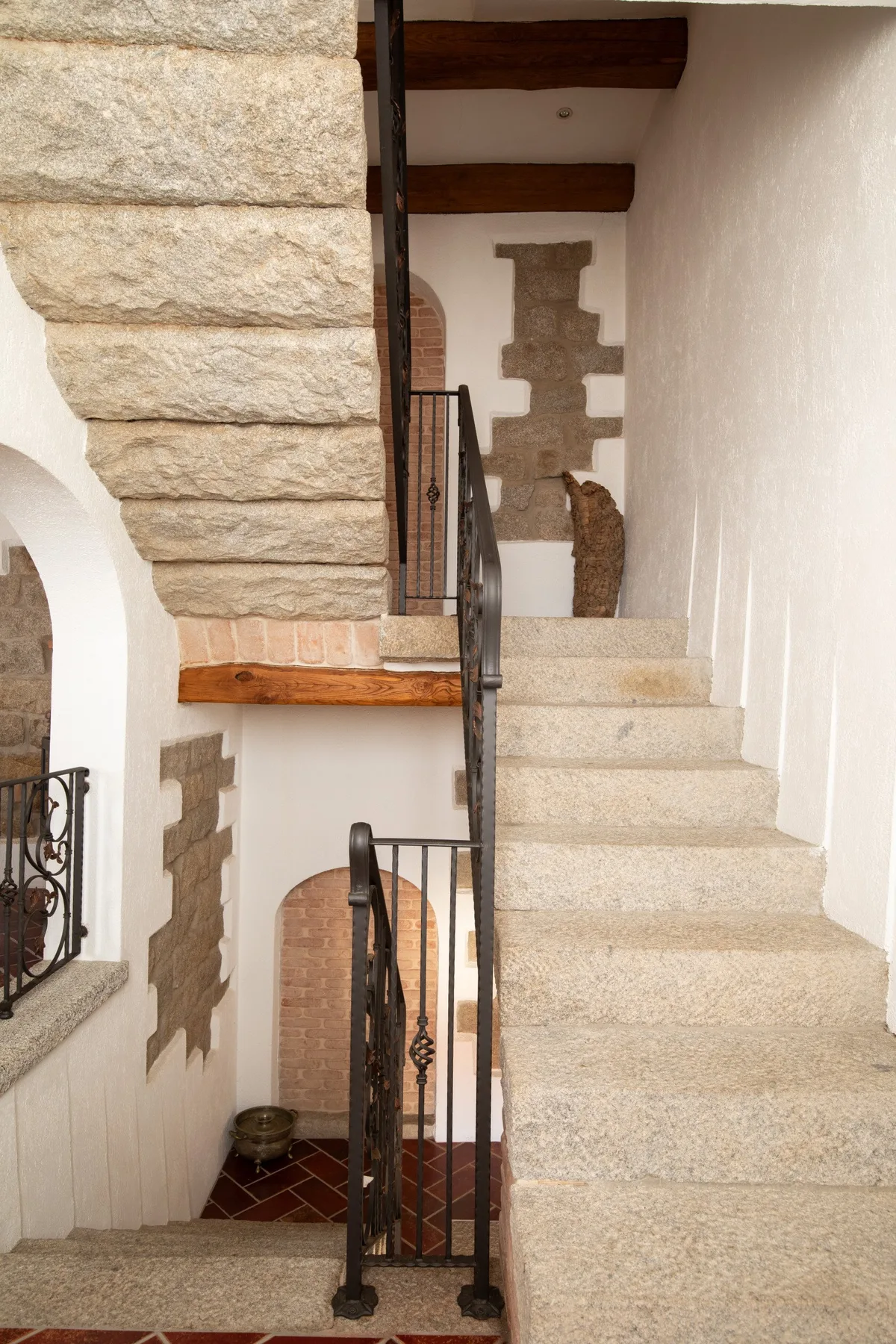 Una escalera de piedra con barandales de metal oscuro sube por un interior blanco.