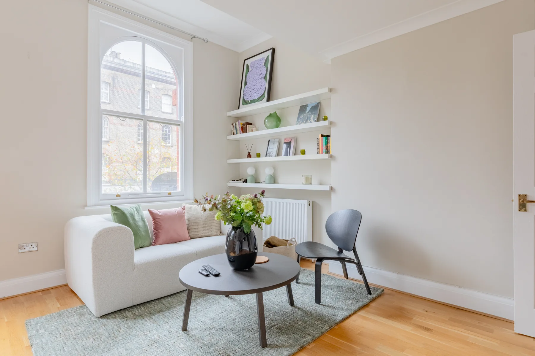A bright sitting room with a sofa, coffee table, and wall shelves.