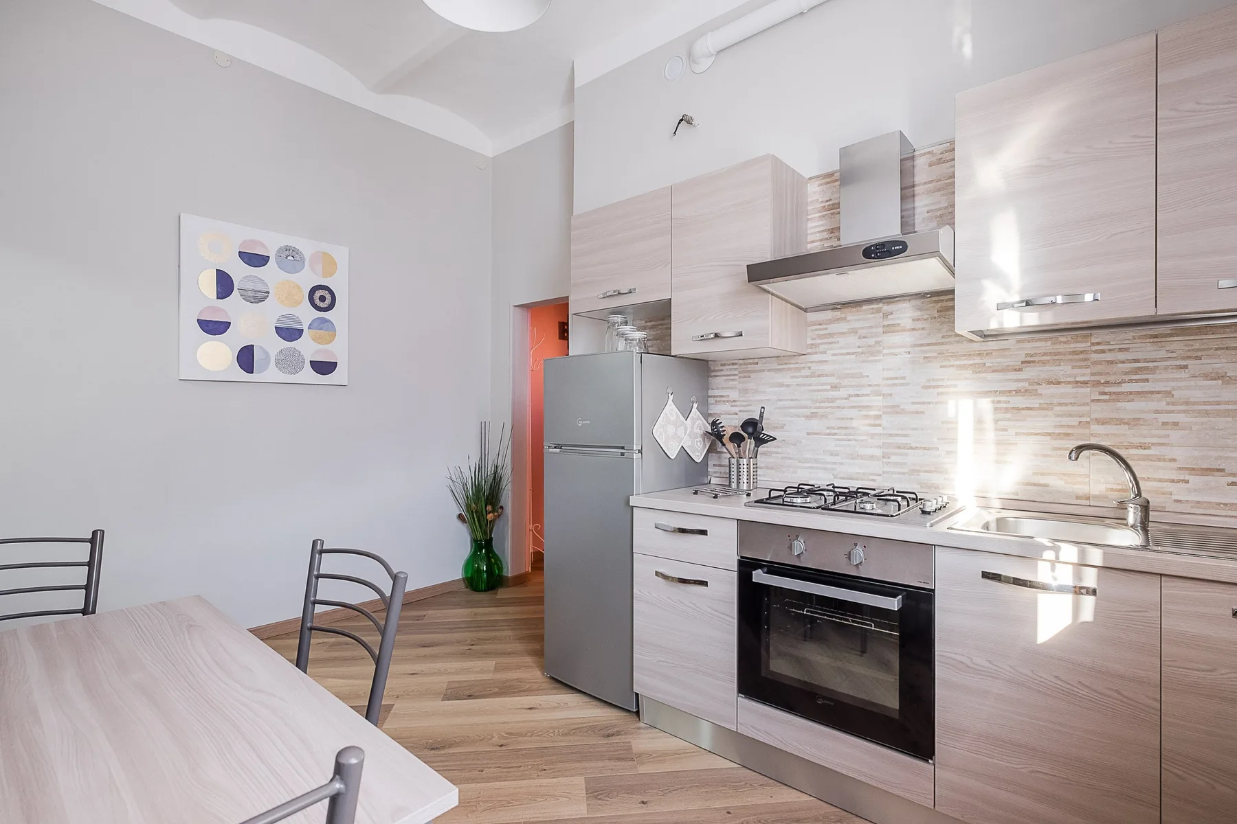A bright kitchen with pale cabinets, a dining table, and a refrigerator.