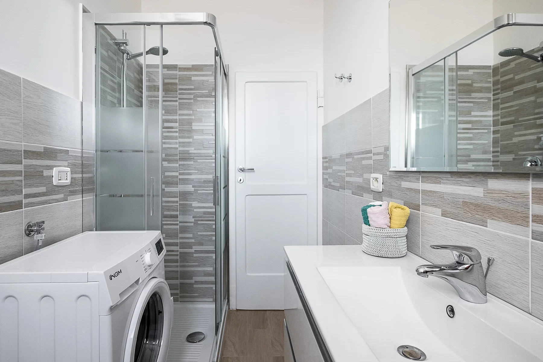 A tiled bathroom with a shower, washing machine, and sink.