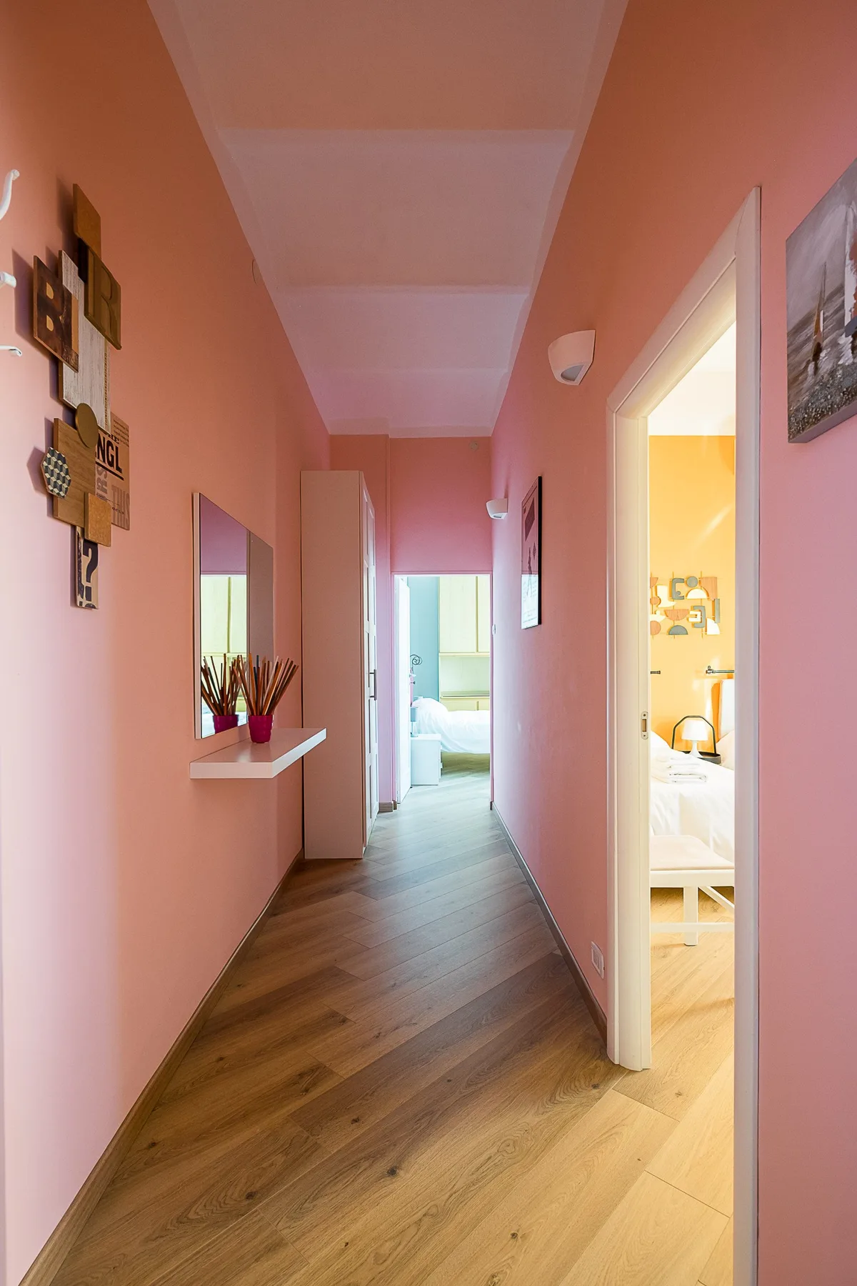 A pink hallway with wood flooring leads to bright rooms.
