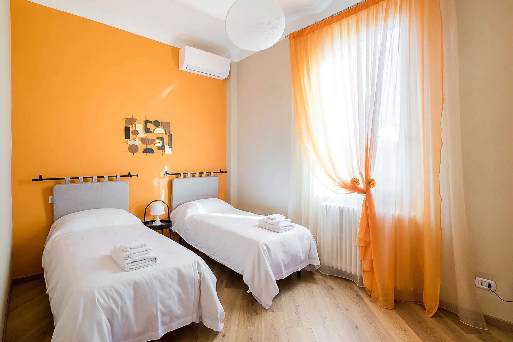 A bright bedroom with twin beds and orange curtains.