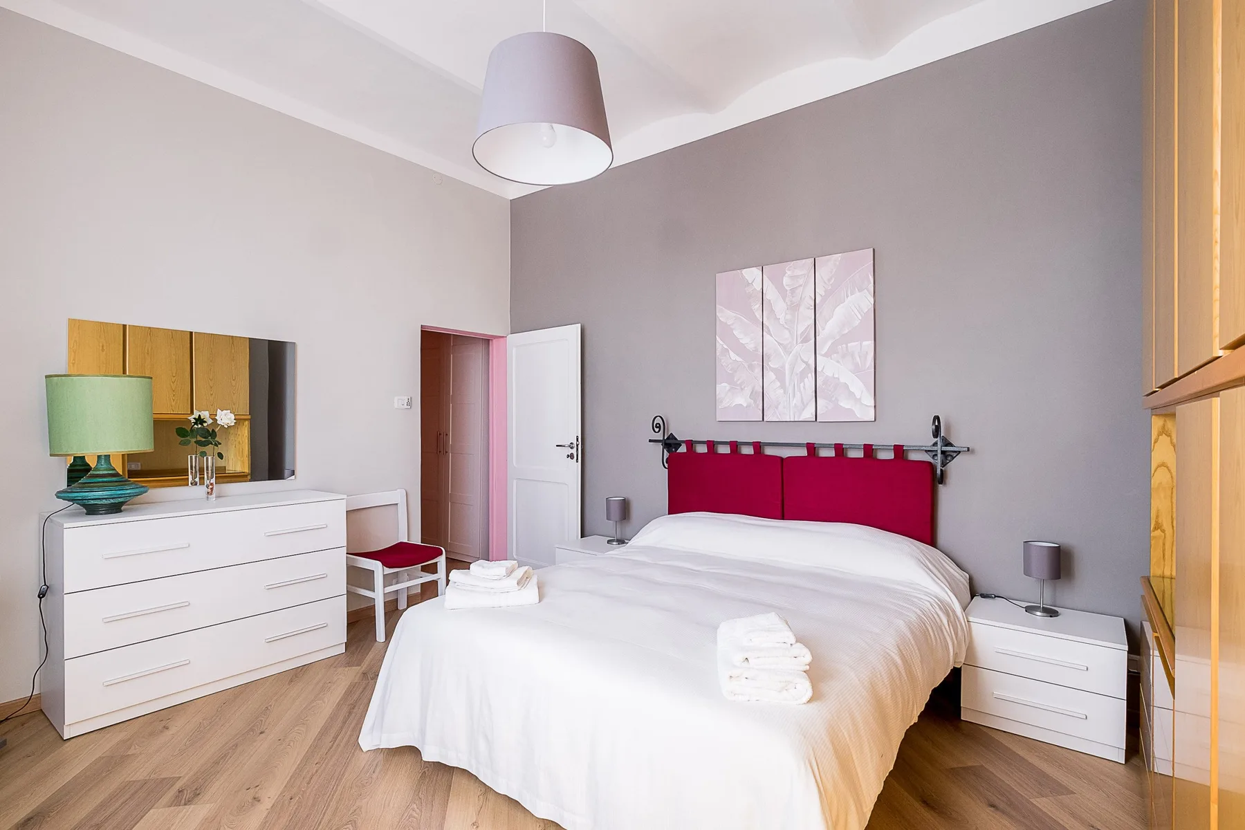 A bedroom with a bed dressed in white linens and a red headboard.