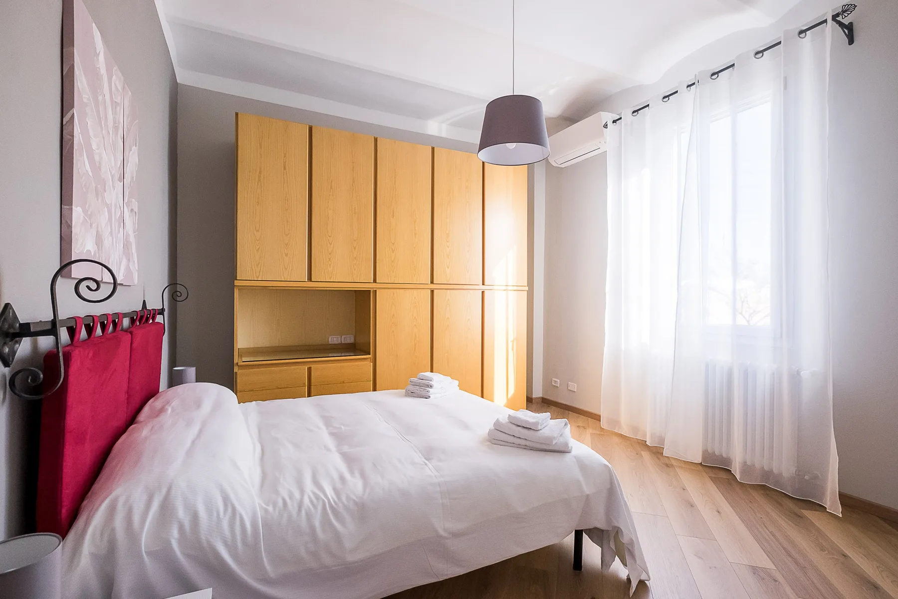 A bedroom with a neatly made bed and wooden built-in cabinets.