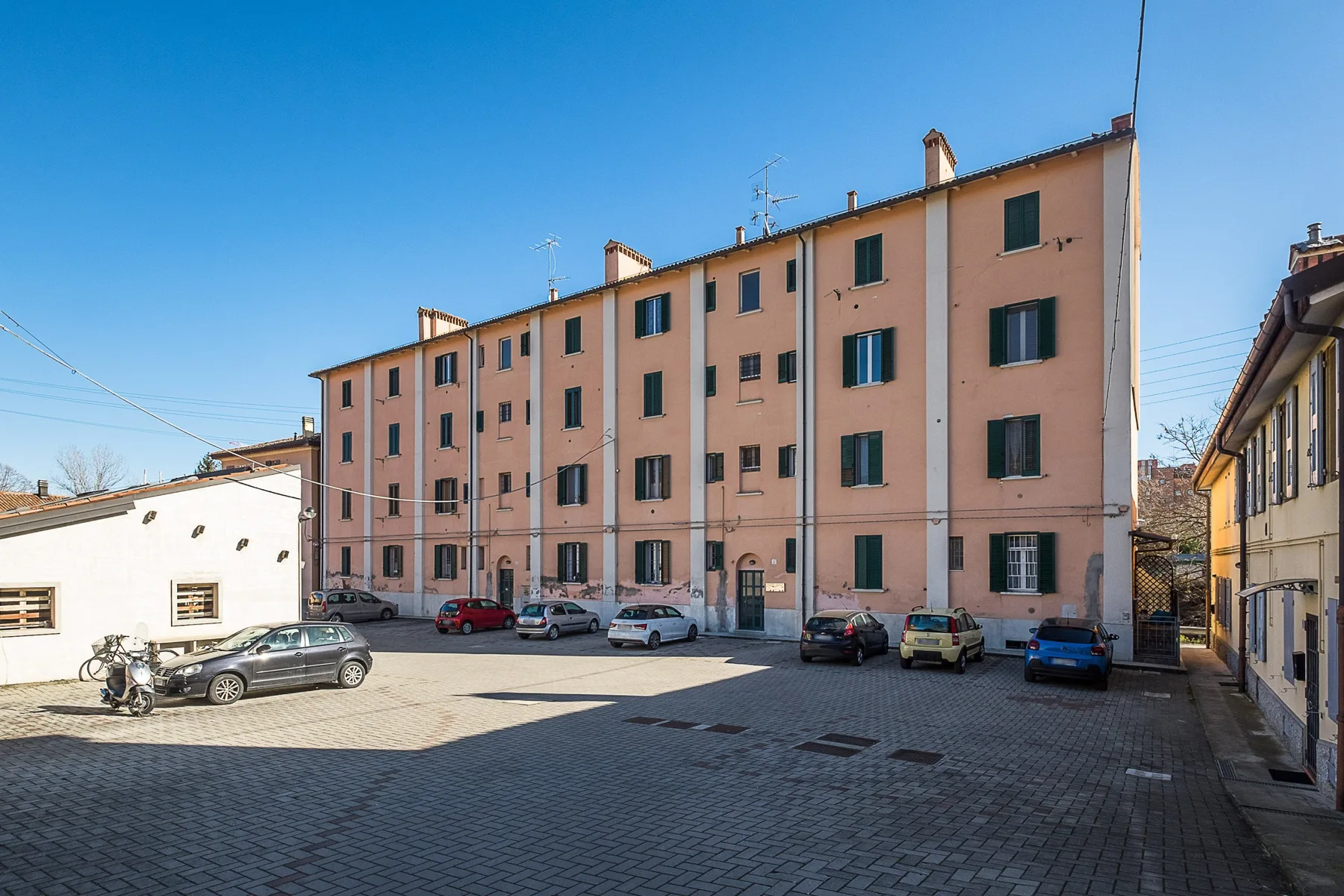 A paved parking area sits in front of a long pink apartment building.