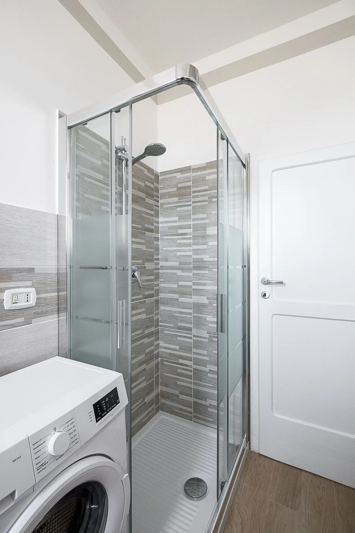 A compact bathroom with a glass shower and a washing machine.