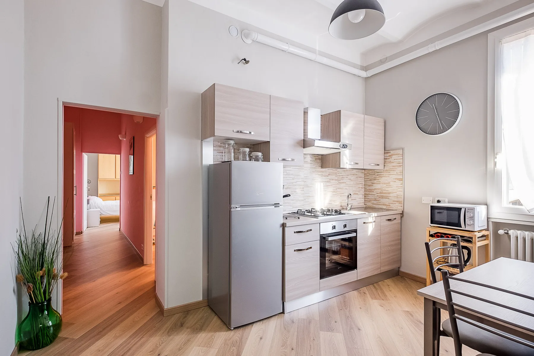 A bright kitchen with light cabinetry, a refrigerator, and a dining table.