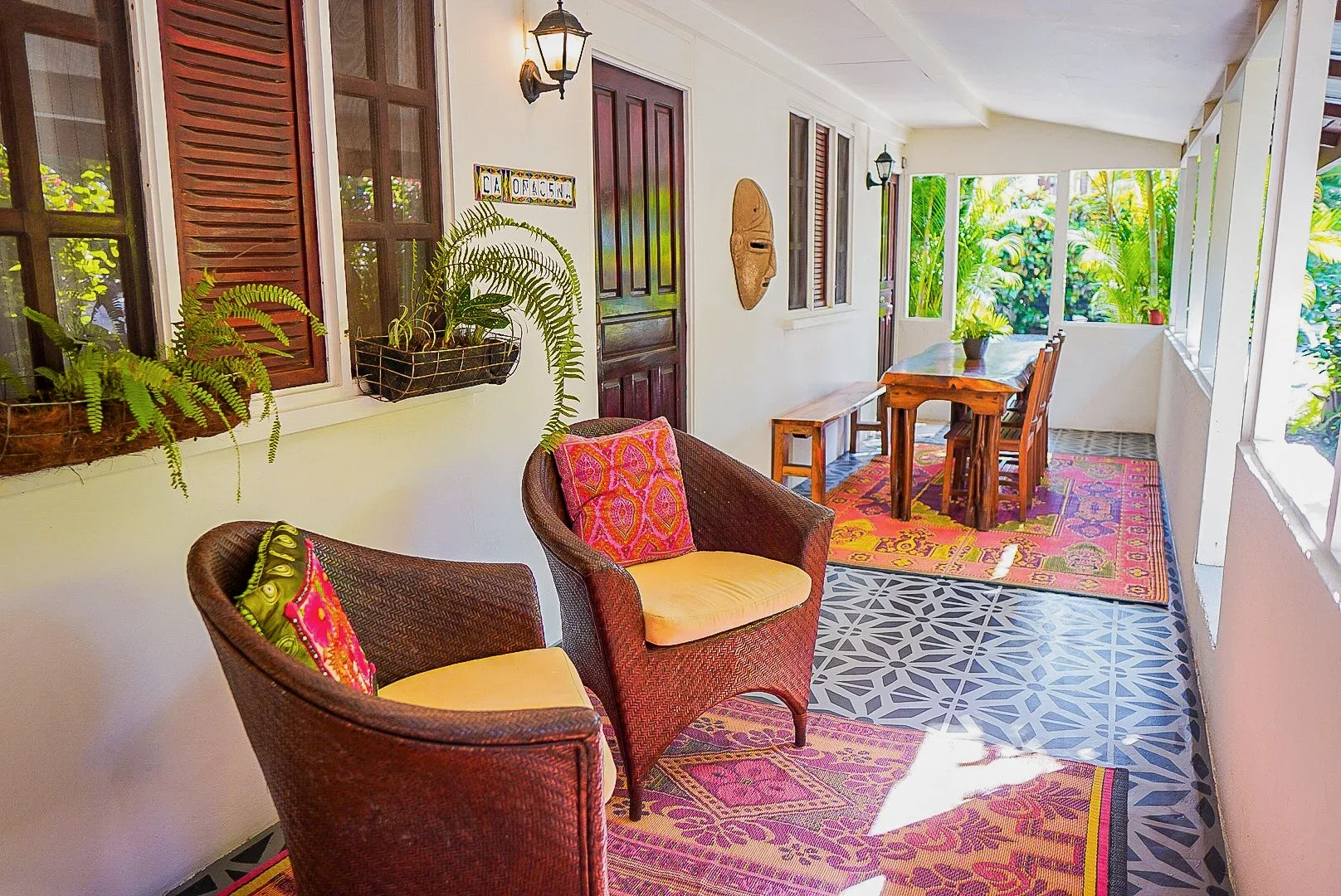 Enclosed porch with seating, a dining table and tropical greenery.