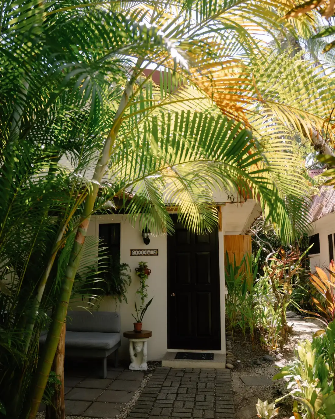 Entrance to a cottage set among tropical plants, with outdoor seating.