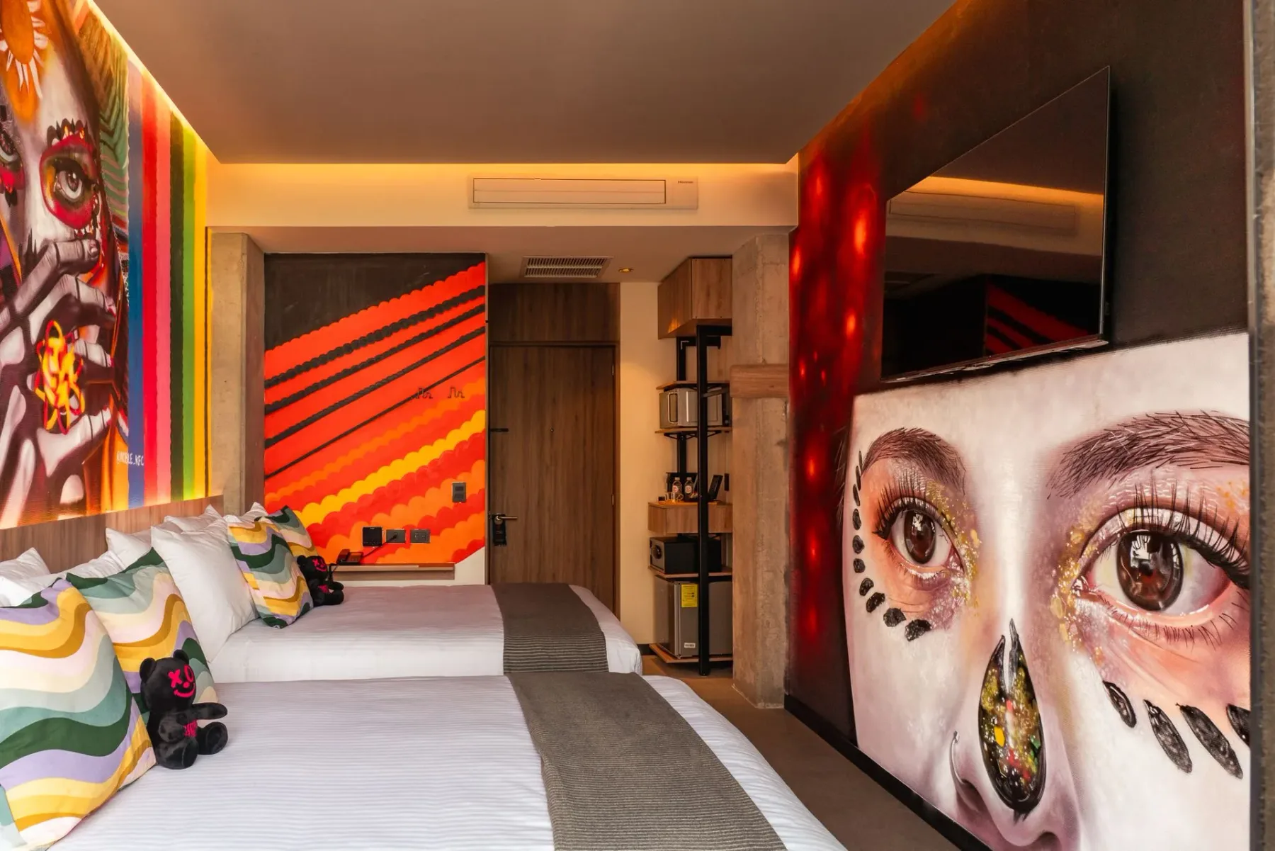 Hotel room with colorful artwork, a large bed, and a wall-mounted TV