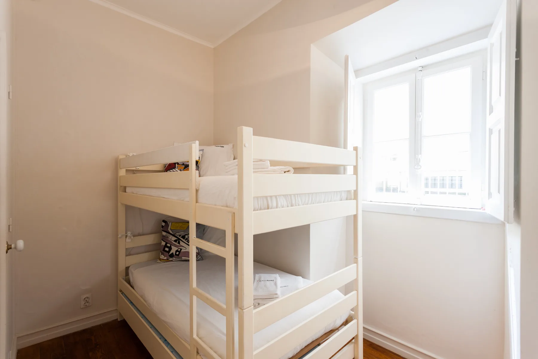 Un dormitorio luminoso con una litera de madera junto a una ventana grande.