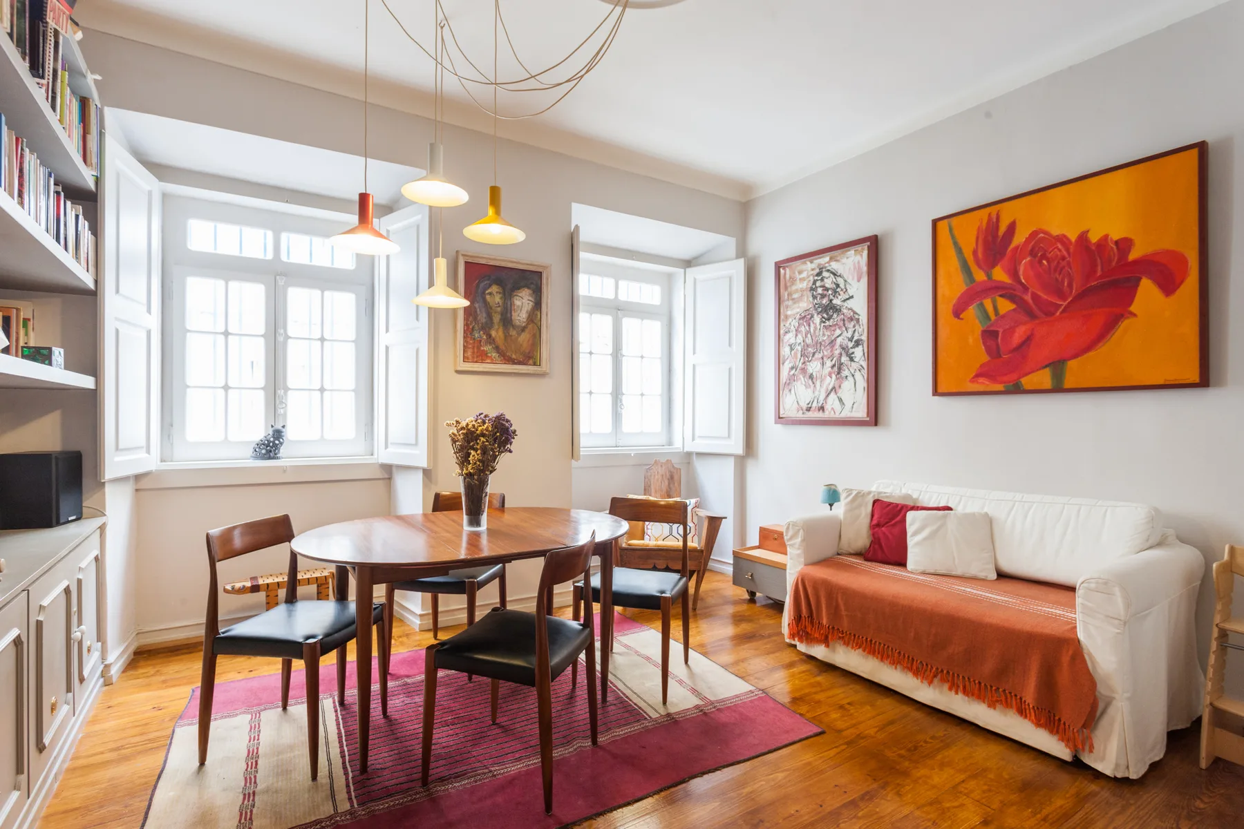 Una sala de estar y comedor luminosa con una mesa de madera y obras de arte coloridas.