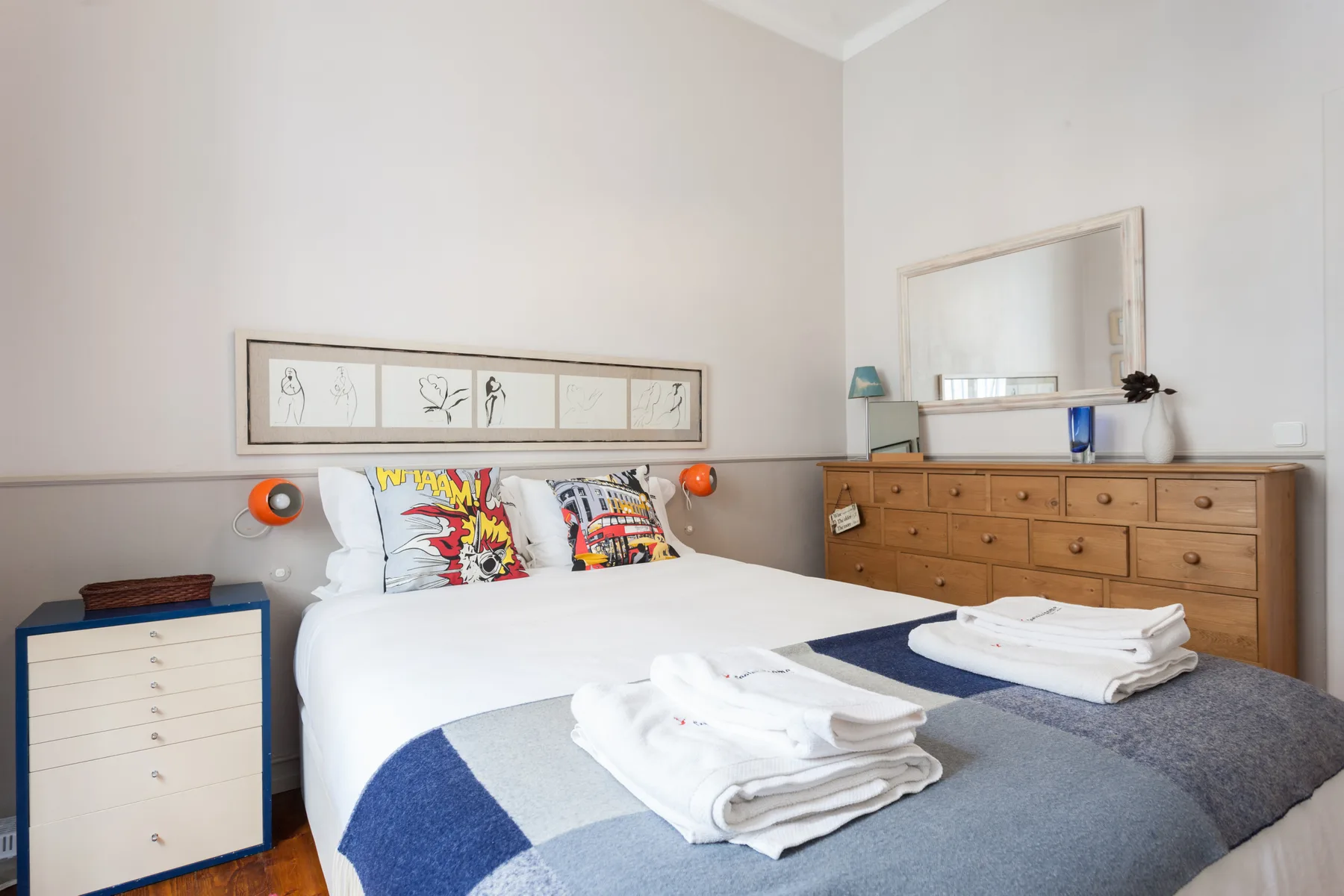 Un dormitorio luminoso con una cama bien tendida y una cómoda de madera.