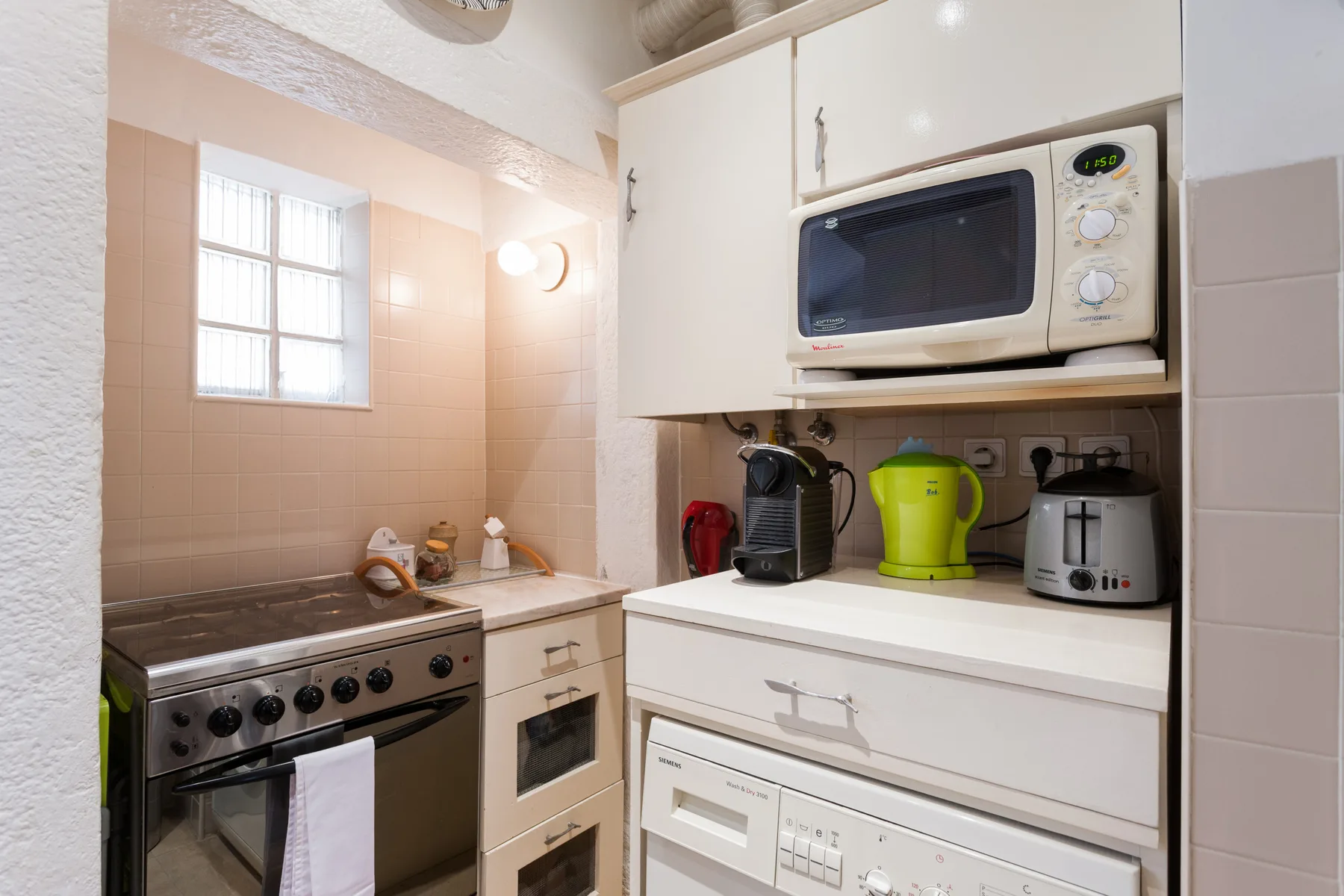 Una cocina compacta con estufa, microondas y pequeños electrodomésticos sobre la encimera.