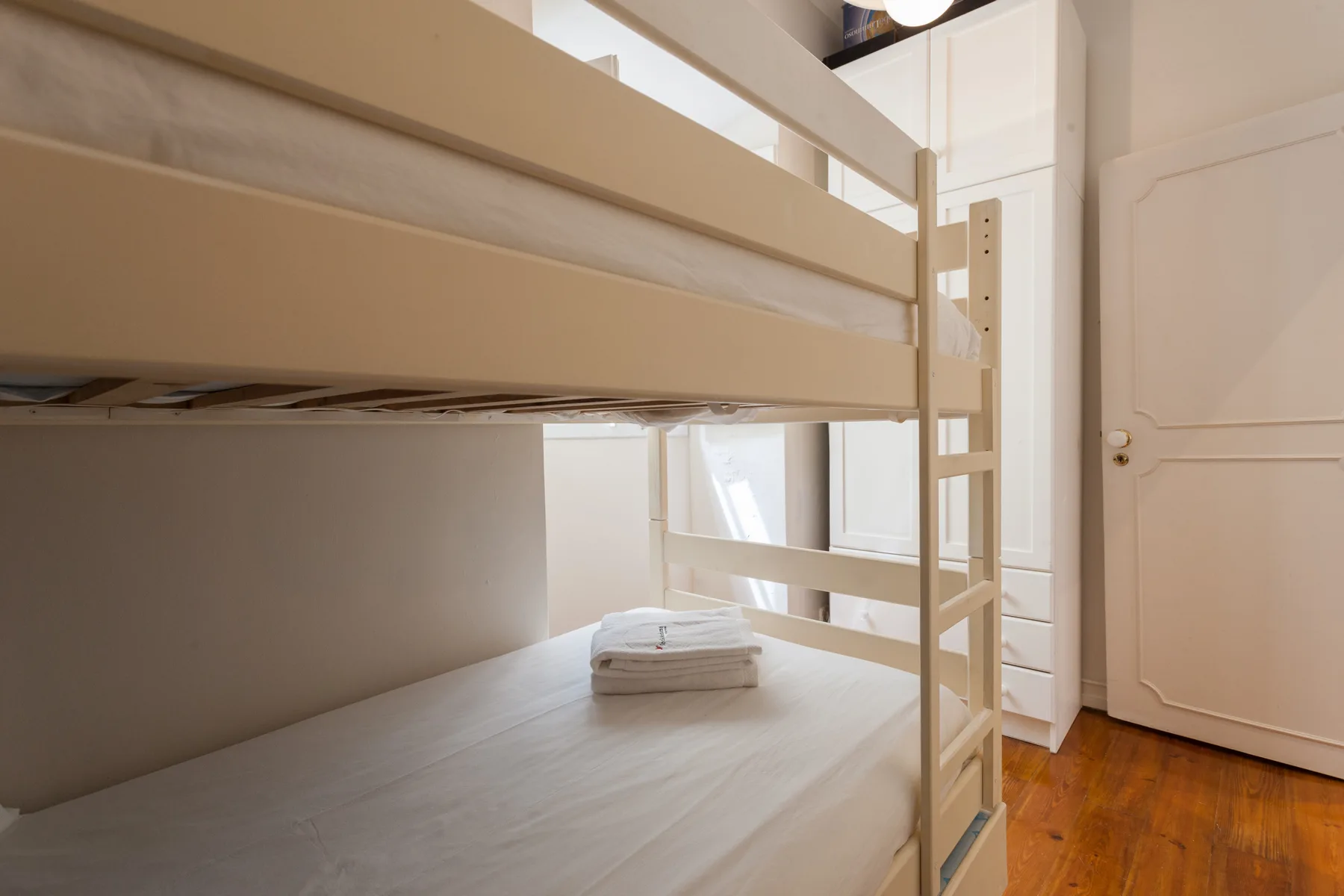 Un dormitorio con una litera blanca y una toalla doblada en la cama inferior.