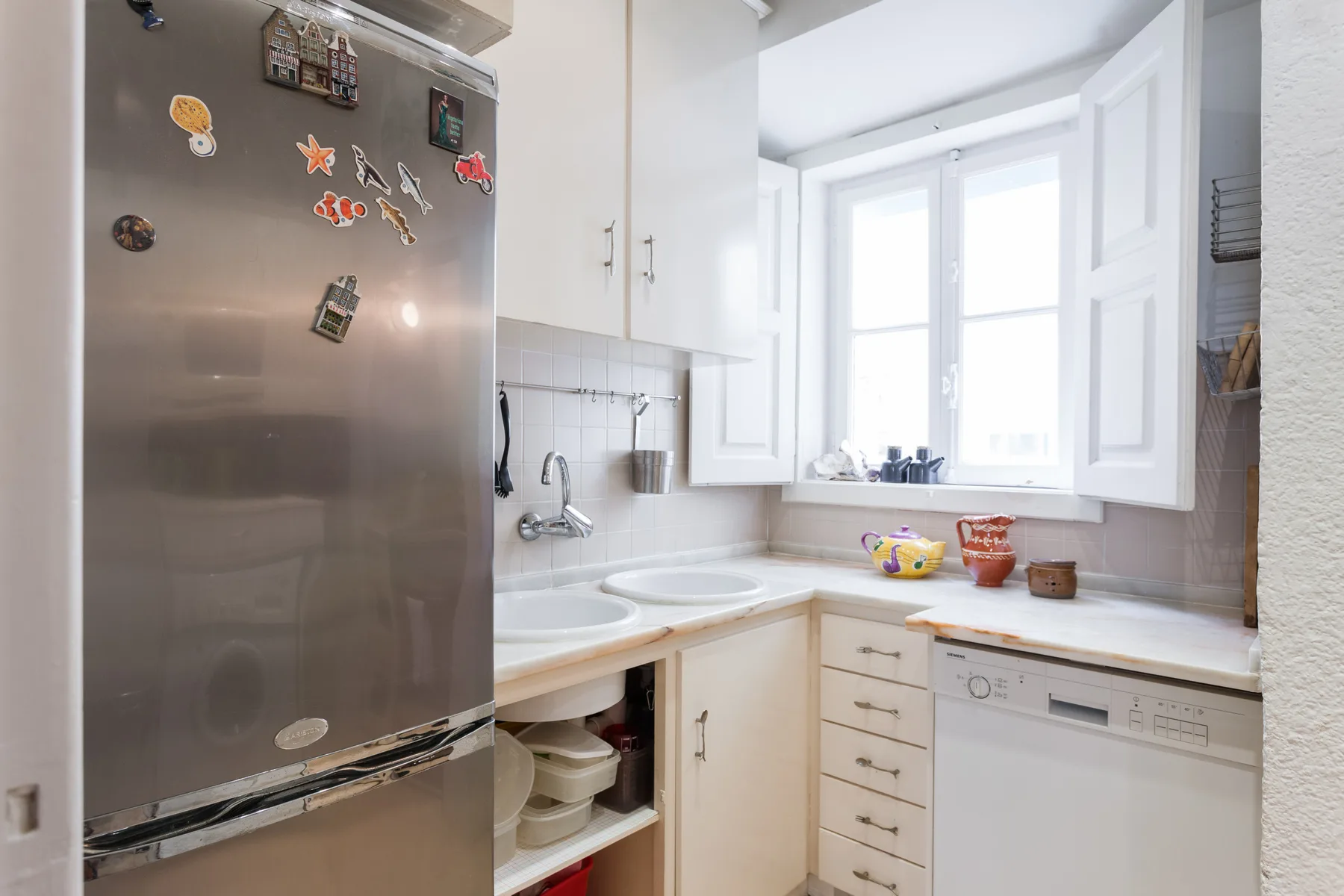 Una cocina luminosa con armarios blancos, un refrigerador y un lavavajillas.