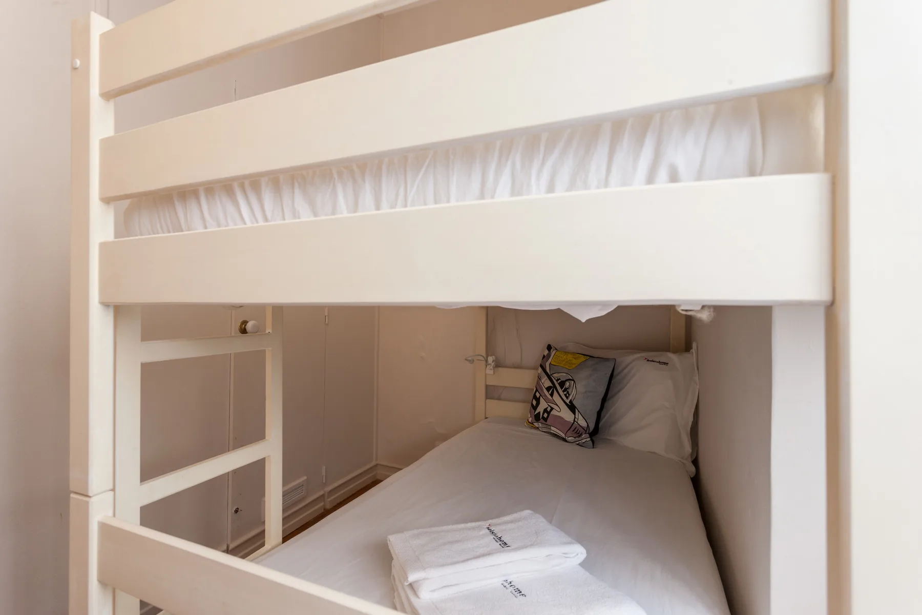 Una zona para dormir compacta con una cama bajo una litera blanca.