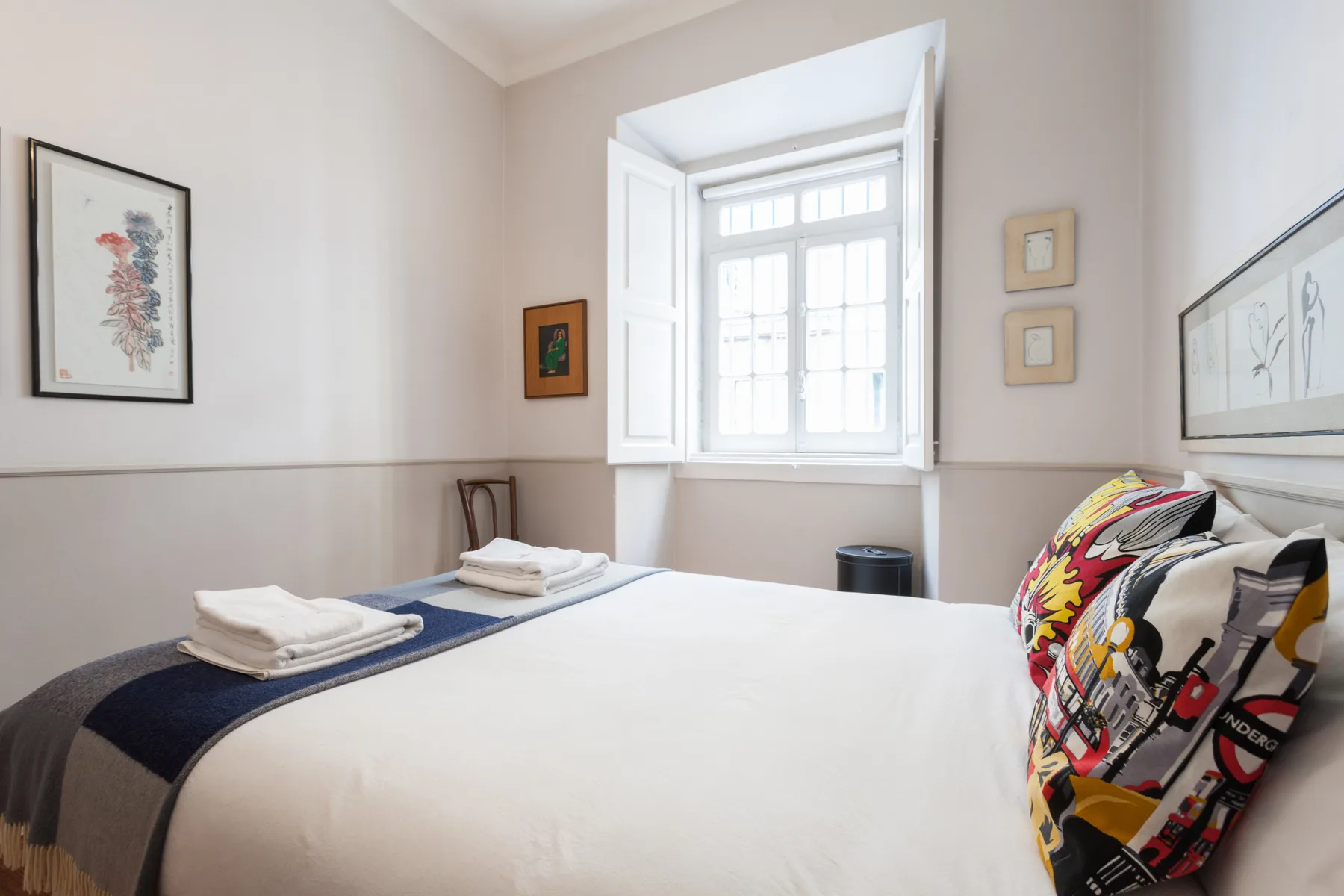 Un dormitorio luminoso con una cama bien hecha bajo una ventana grande.