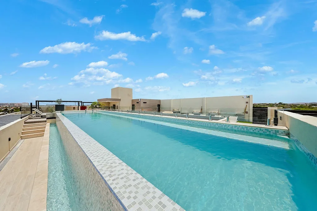 A rooftop pool stretches across a sunny deck, surrounded by modern architecture and open horizons—your perfect spot to unwind above it all.