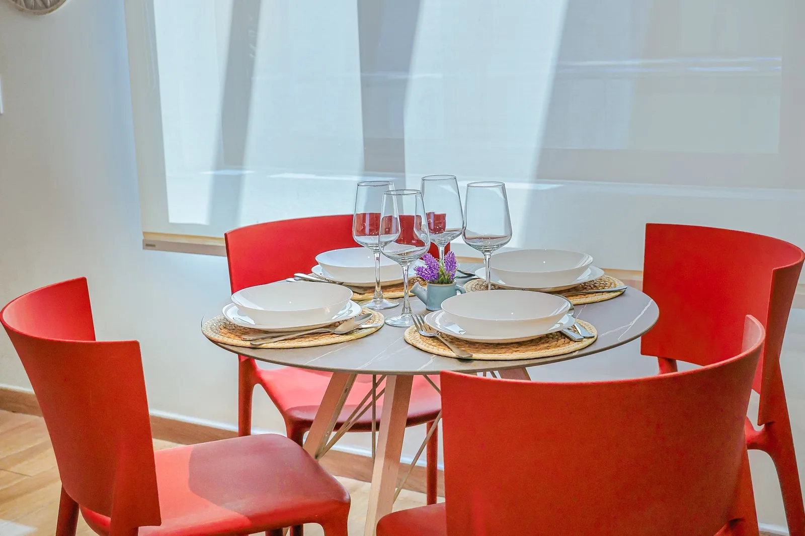 A bright dining table awaits your meals, set with crisp white dishes and modern coral-red chairs that add warmth to your dining experience.