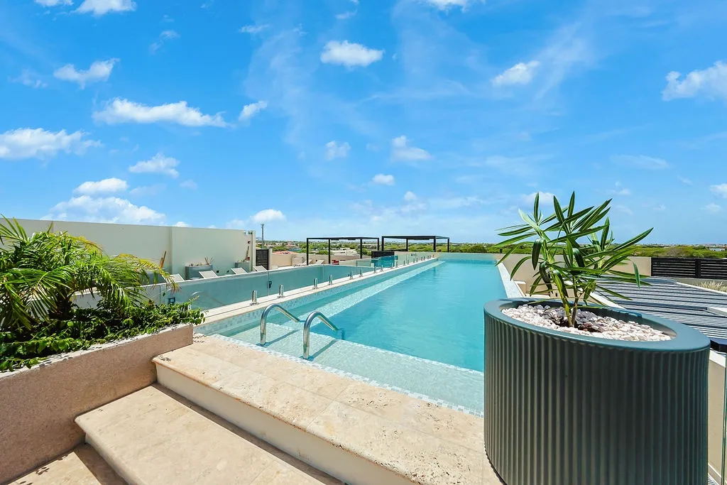 This rooftop pool offers a peaceful retreat with tropical greenery and endless blue skies. Comfortable loungers await, framed by lush landscaping and open views of the natural surroundings.