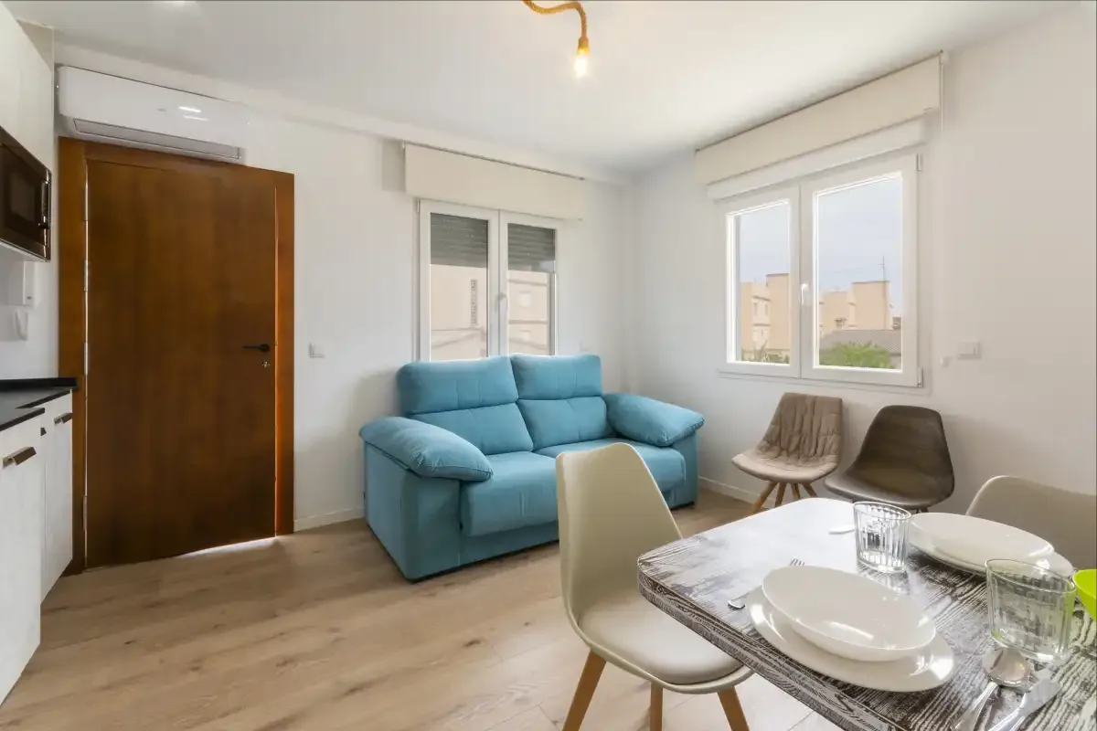Una luminosa zona de estar y comedor con asientos azules, ventanas y una mesa de comedor.