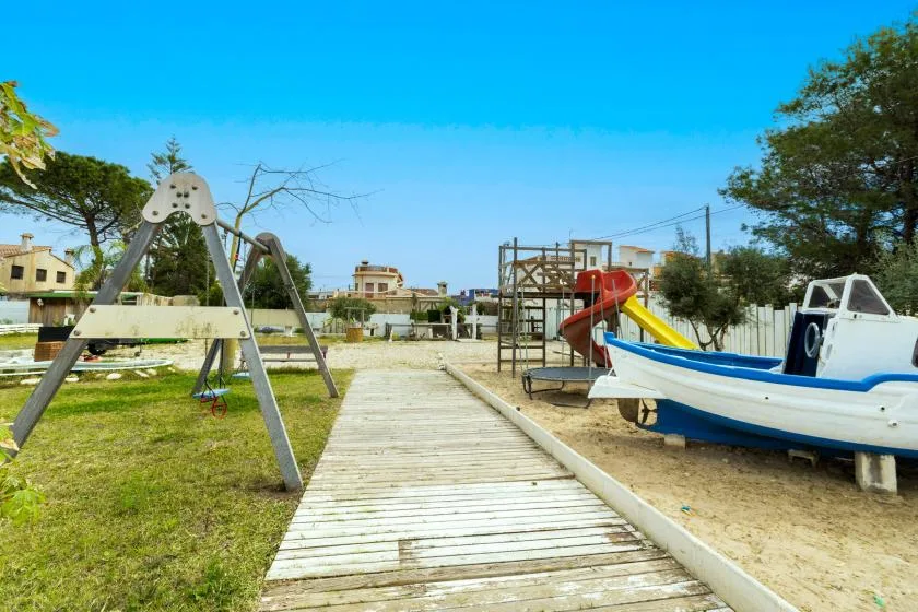 Una zona de juegos al aire libre con un sendero de madera, juegos infantiles y una estructura con forma de barco.