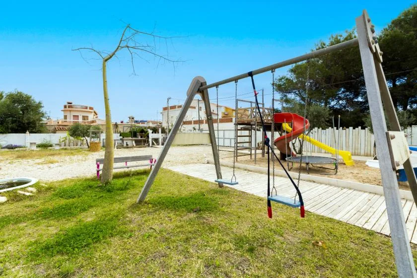 Un parque infantil al aire libre con columpios, estructura para trepar y tobogán sobre césped.