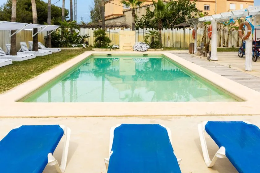 Una piscina al aire libre está bordeada por tumbonas azules y una terraza pavimentada.