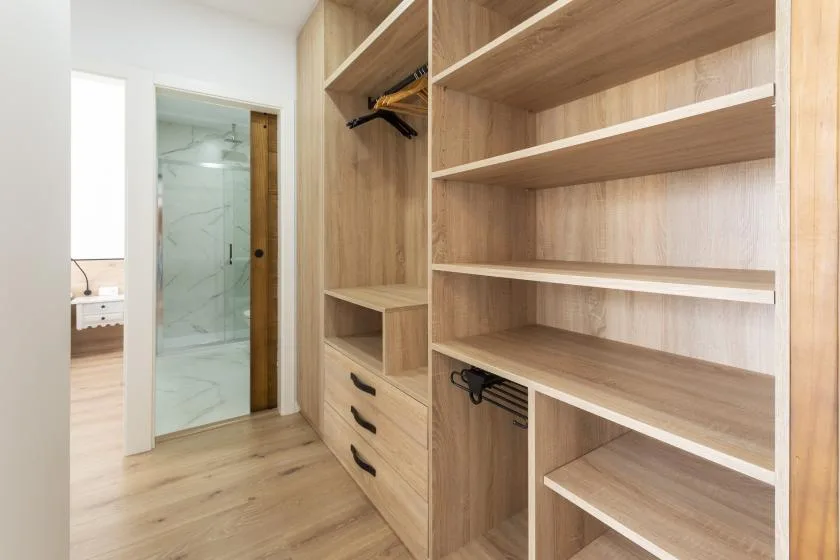Un vestidor con estantes abiertos de madera y cajones junto a una ducha de vidrio.
