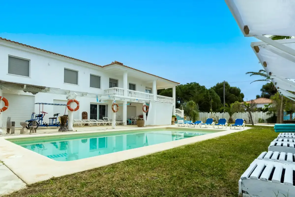 Un edificio blanco de dos plantas da a una piscina y un patio con césped.