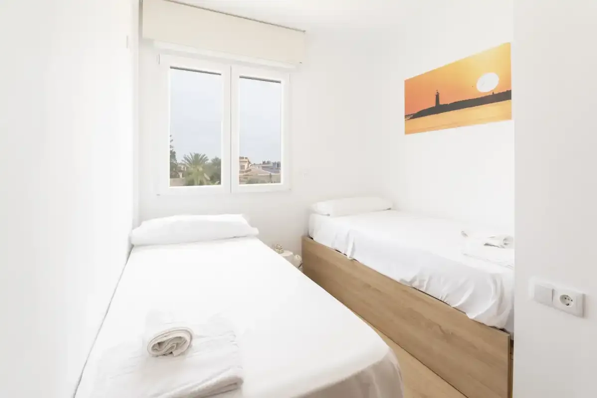 Un dormitorio luminoso con dos camas y una ventana con vistas a palmeras.