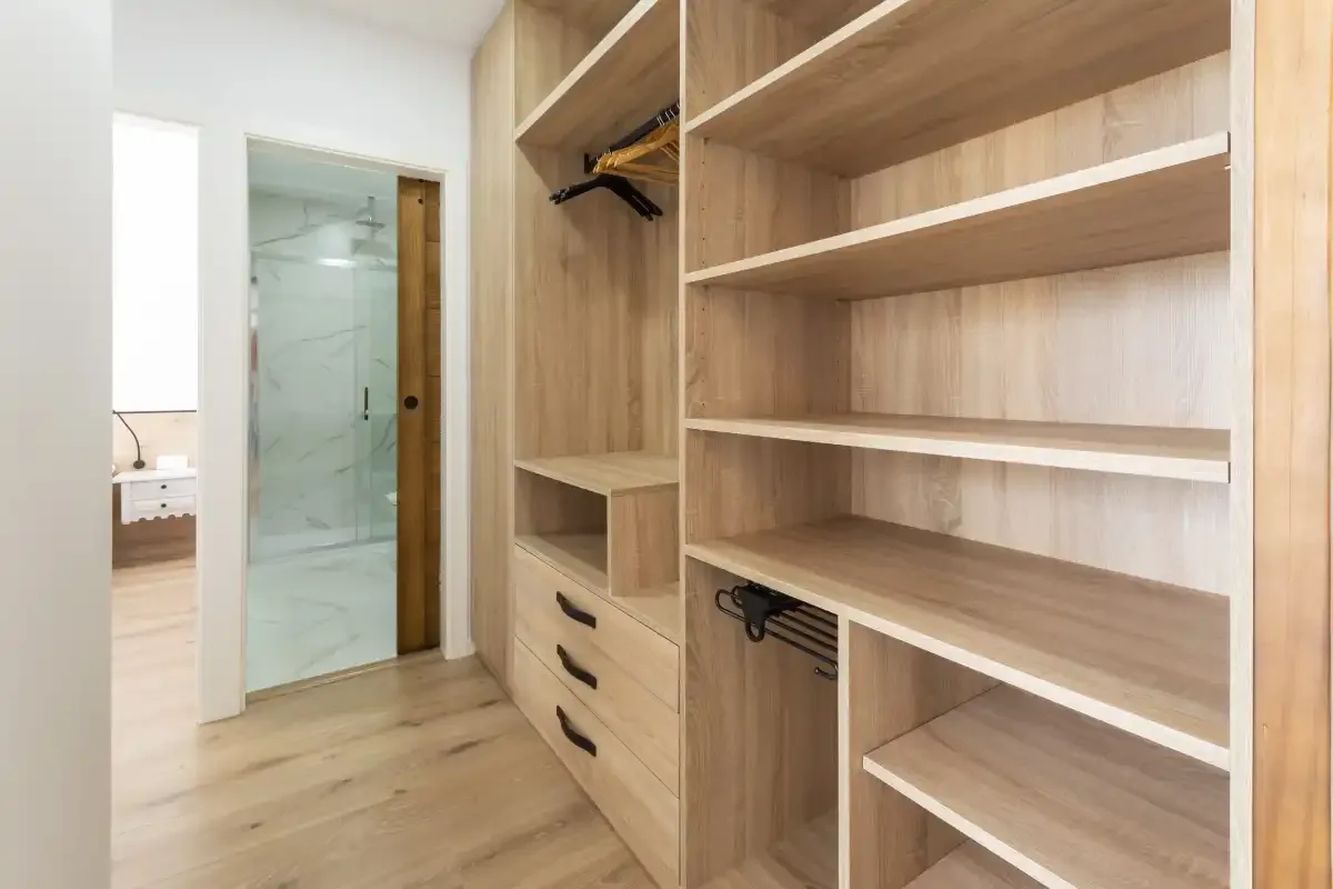 Un vestidor con estantes abiertos de madera y cajones junto a una ducha de vidrio.